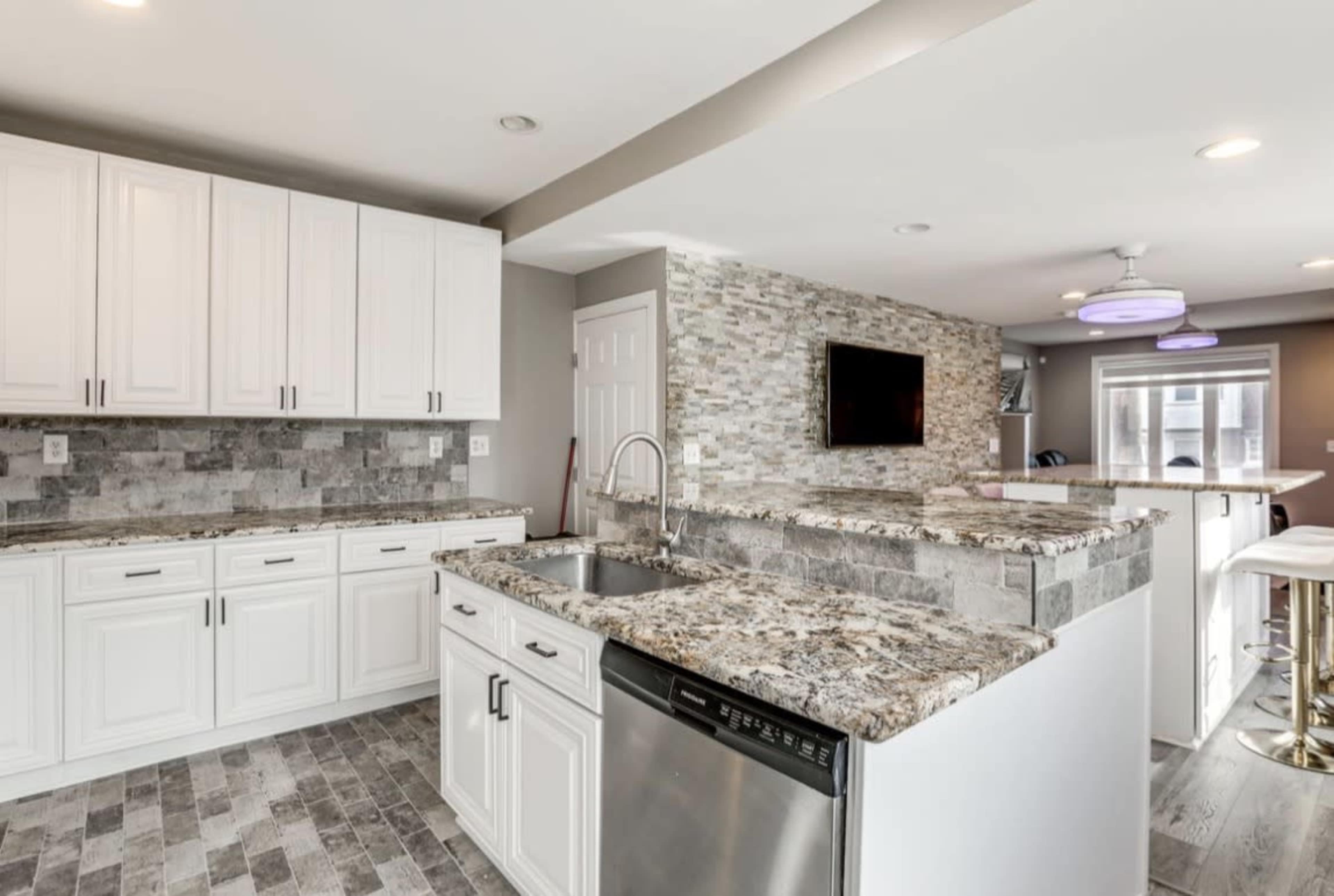 The image shows a modern kitchen featuring white cabinets, a stone backsplash, and a granite countertop with an integrated sink and dishwasher.