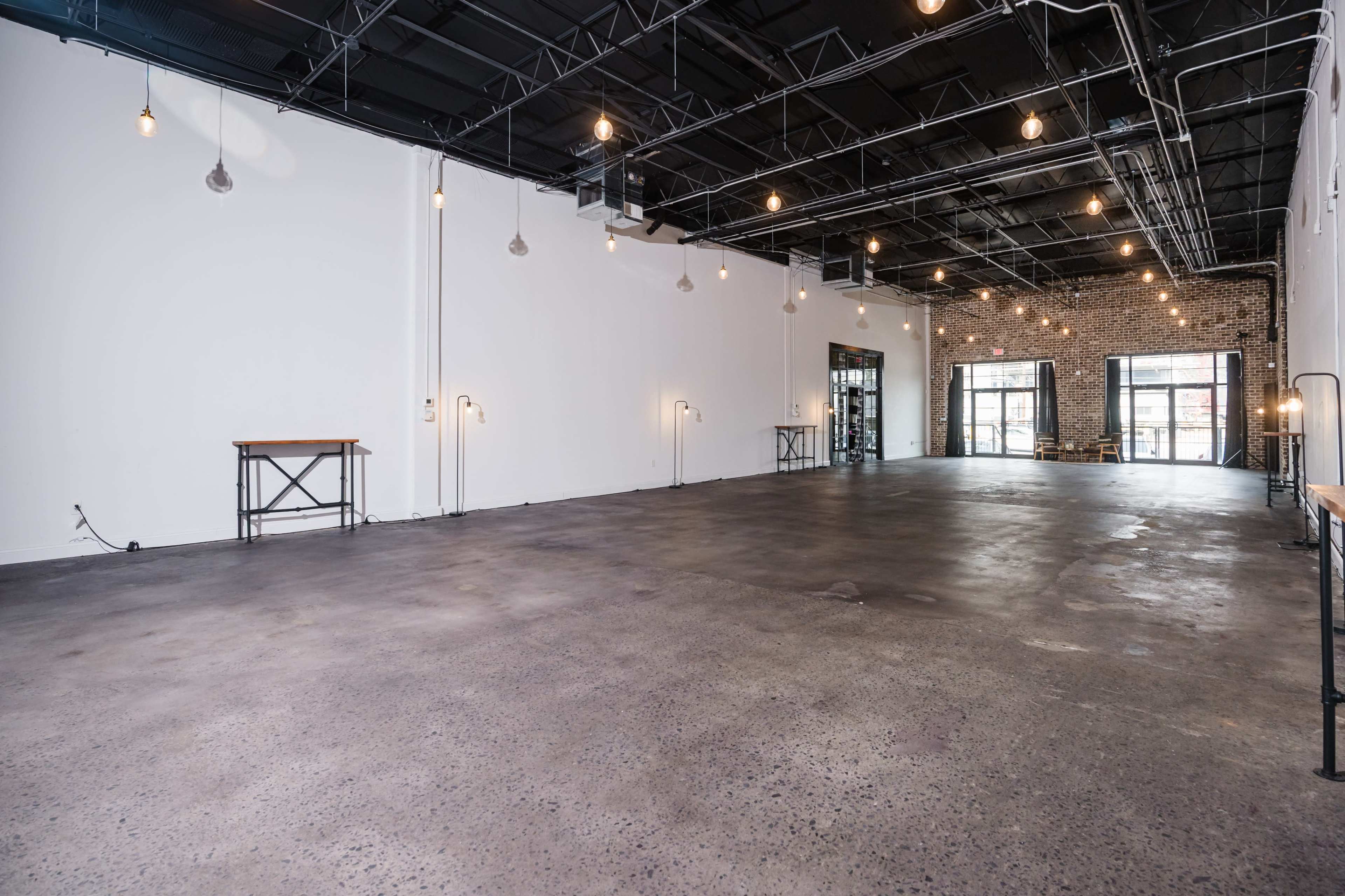 The image shows a spacious, empty interior with exposed brick walls and overhead pendant lighting.