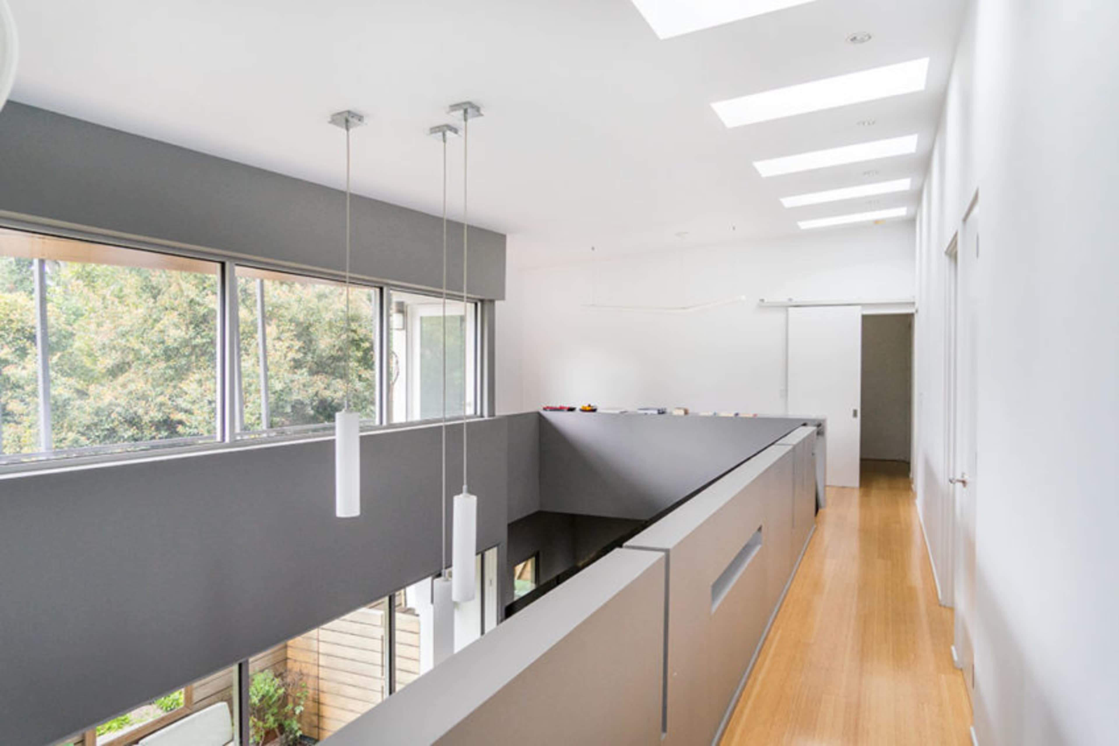 The image shows a modern, open-concept interior space with large windows, a balcony railing, and recessed lighting.
