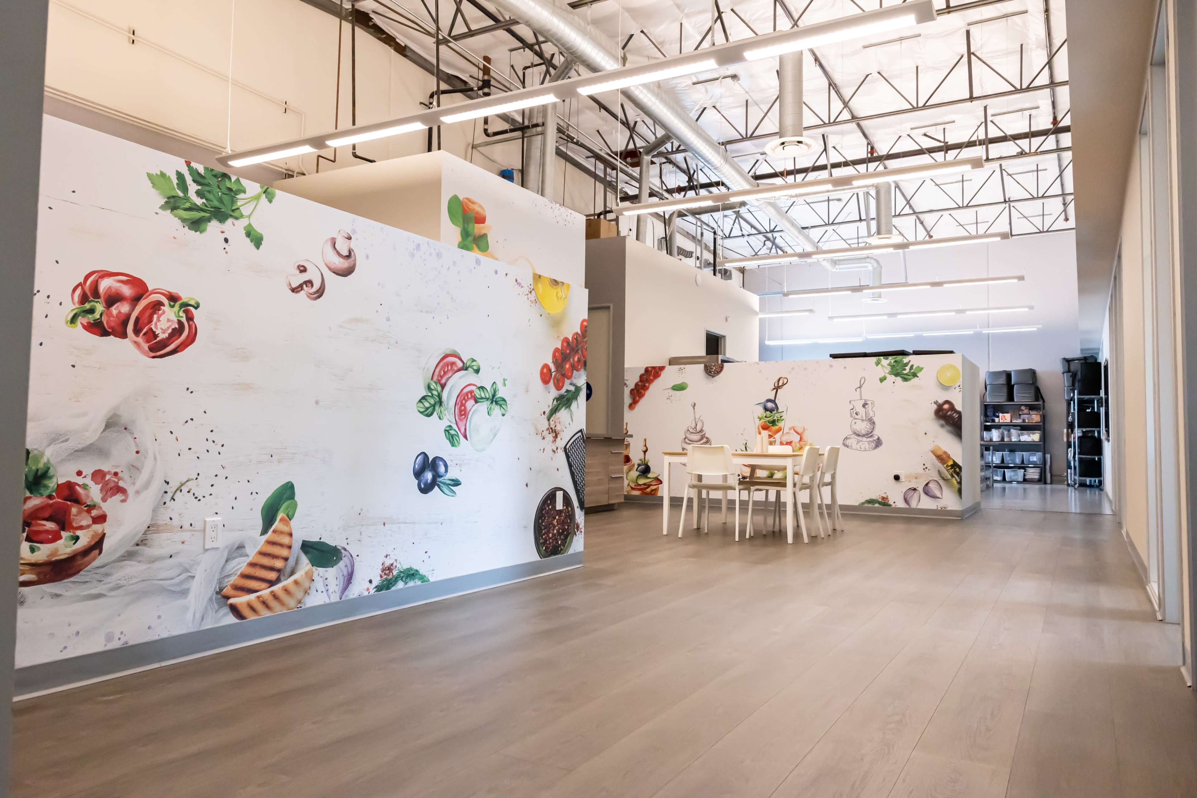 A spacious room with large murals of food items on the walls and a dining area featuring a white table and chairs.
