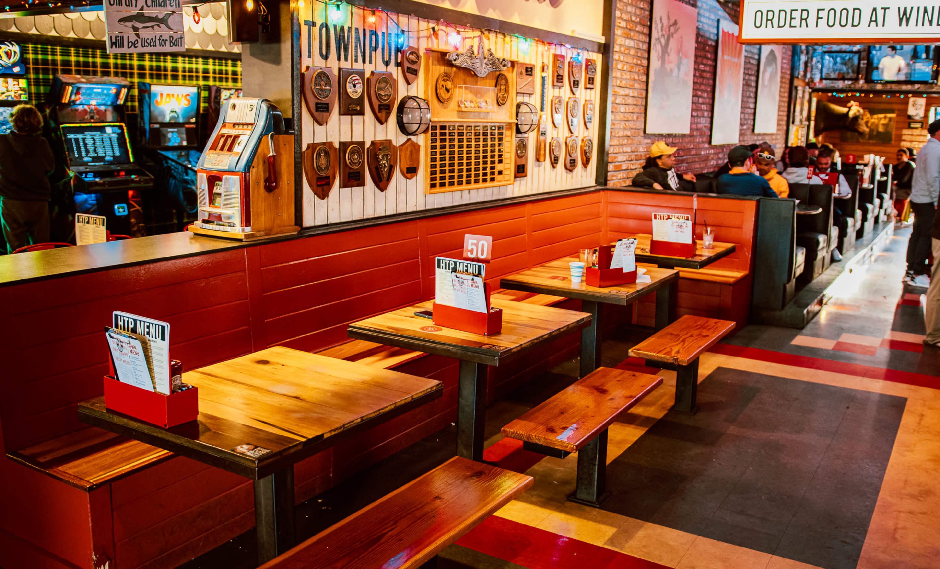 The image shows a casual dining area with wooden tables and benches, decorated with wall plaques and a sign for ordering food.