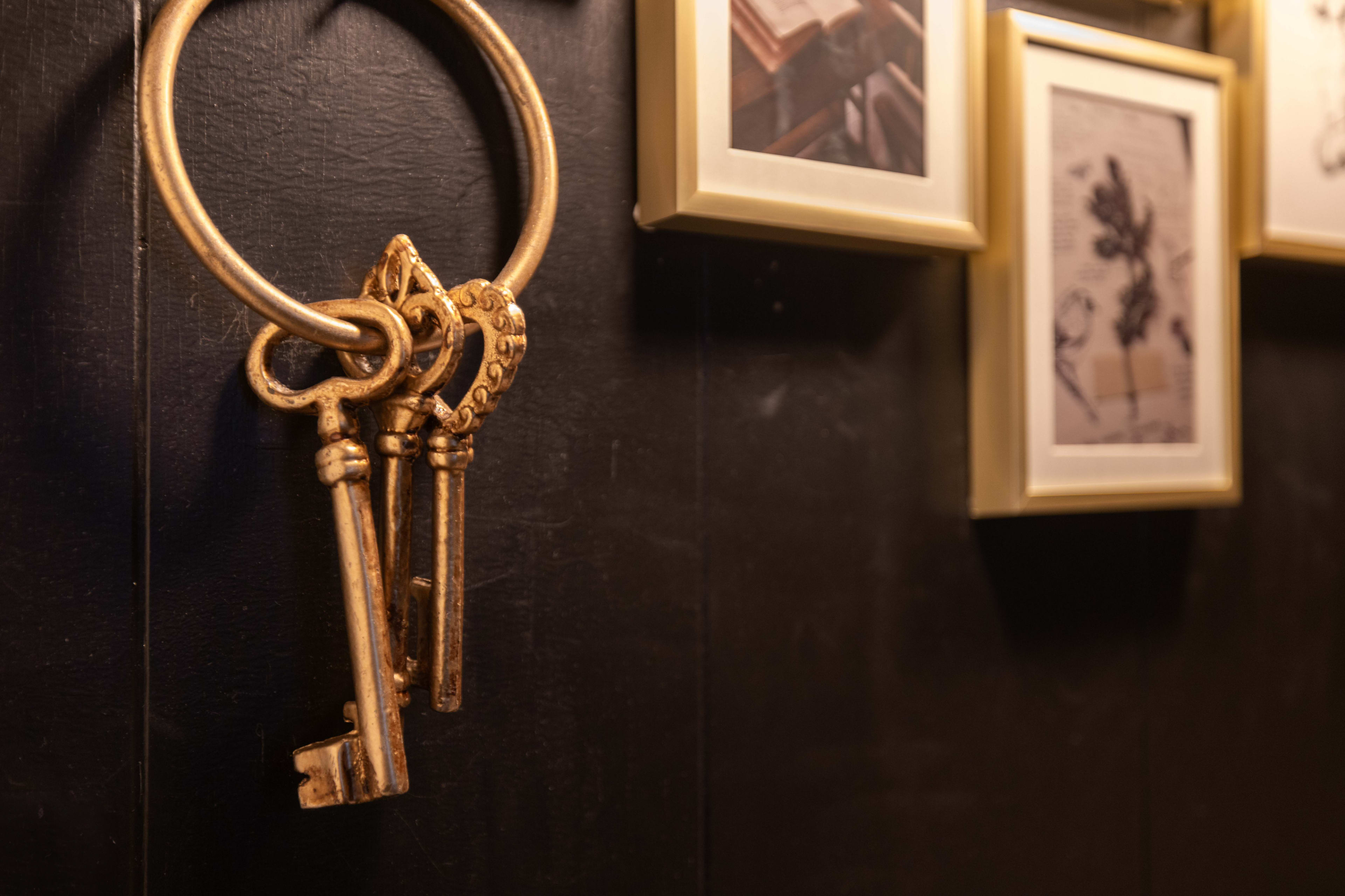 A set of vintage gold keys is hanging from a circular keyring on a dark wall, alongside framed photographs.