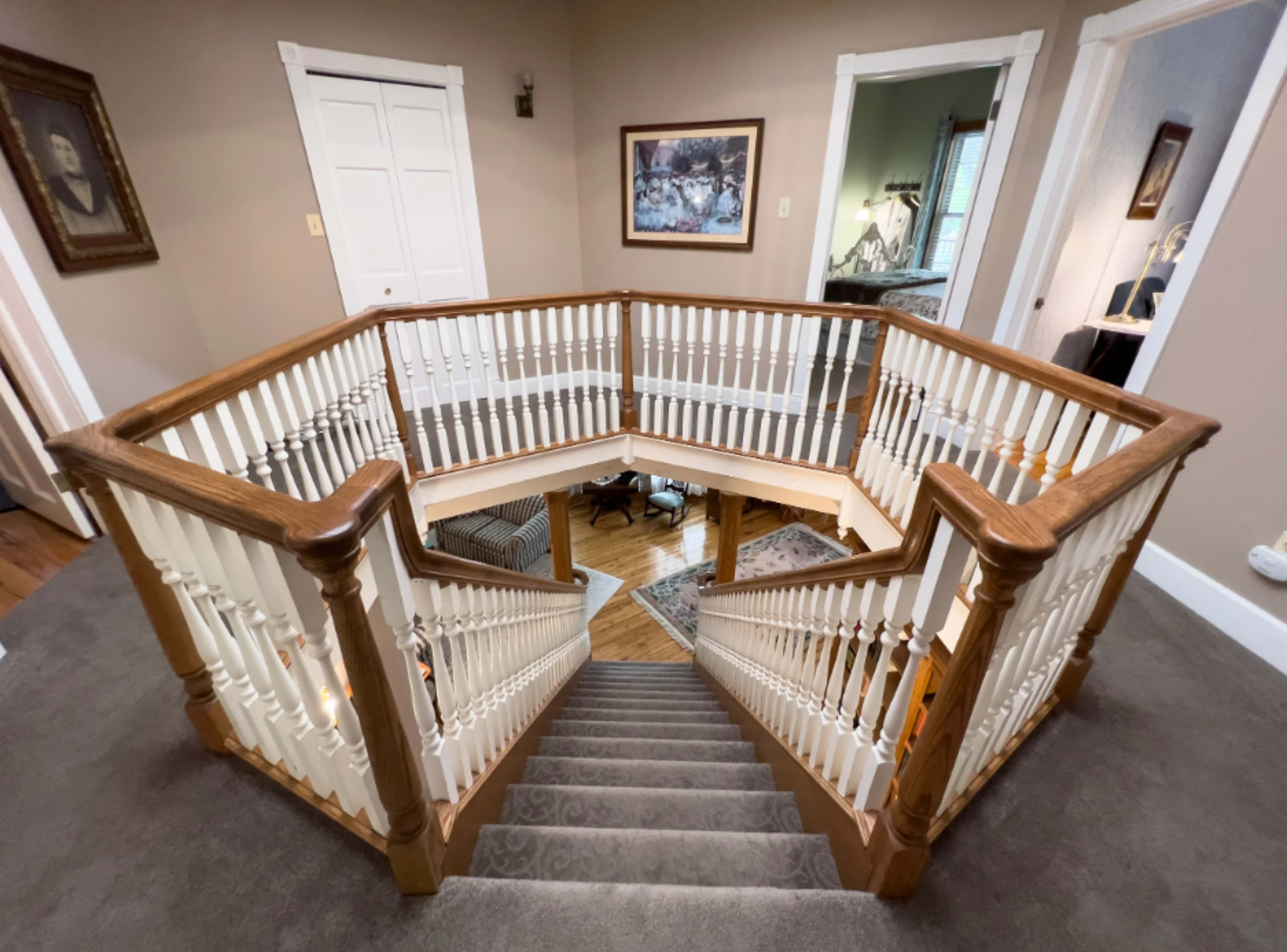 A curved wooden staircase with white balusters leads down to a lower level, surrounded by a landing that features framed artwork and open doorways.