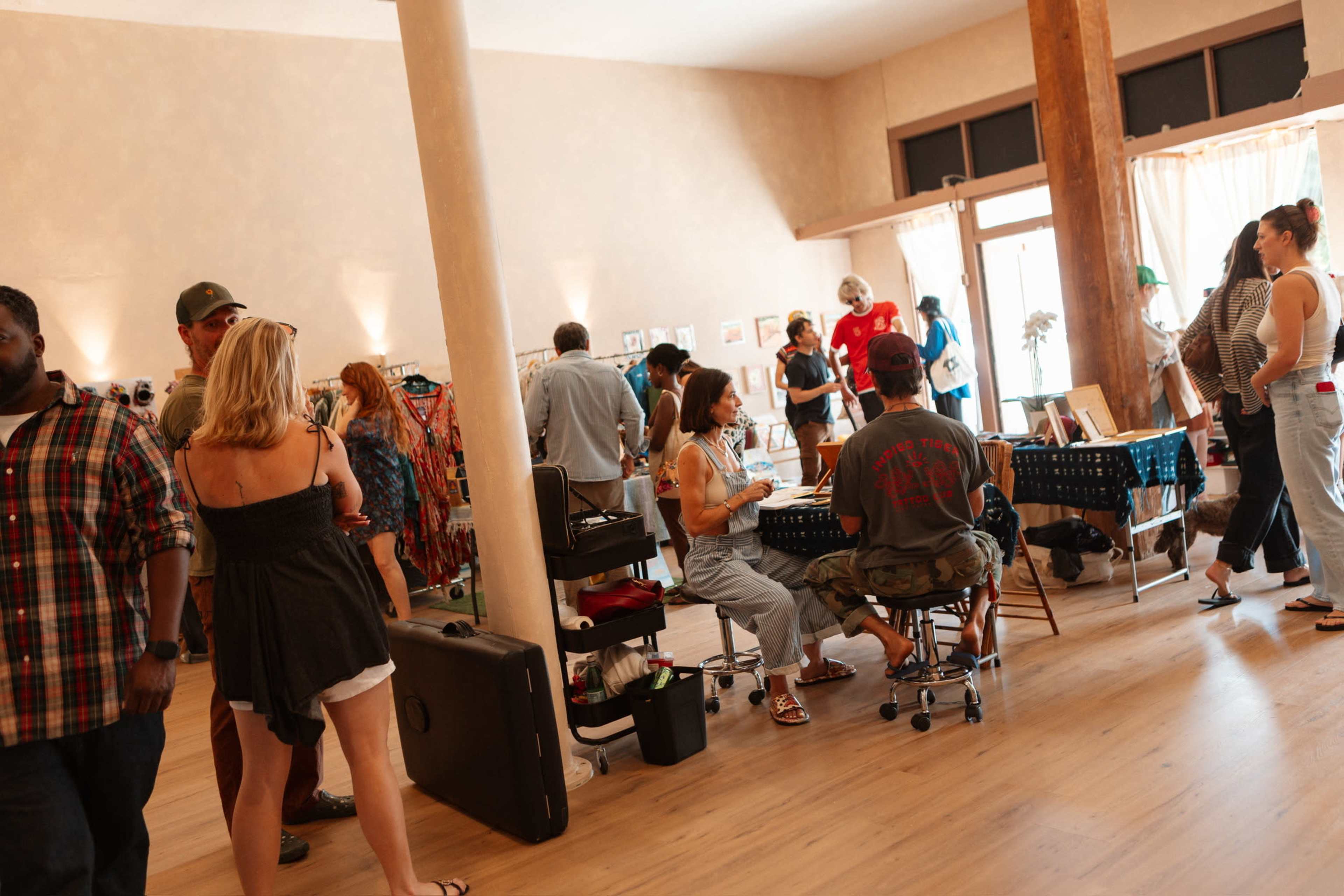 A busy indoor space features several people engaged in various activities, including crafting and conversing, with tables set up around the room.
