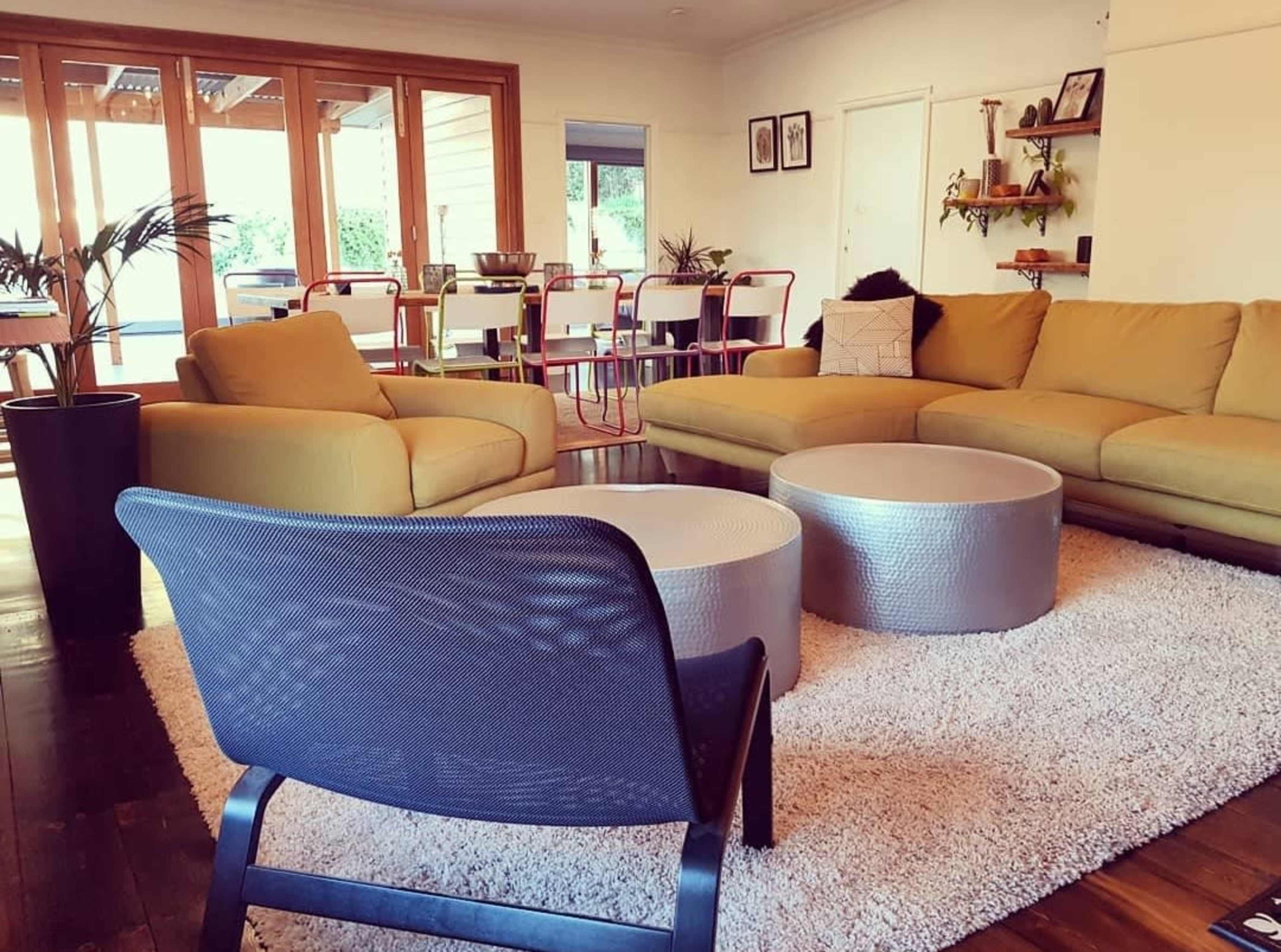 A modern living room features a yellow sofa, circular coffee tables, a textured rug, and large windows leading to an outdoor area.