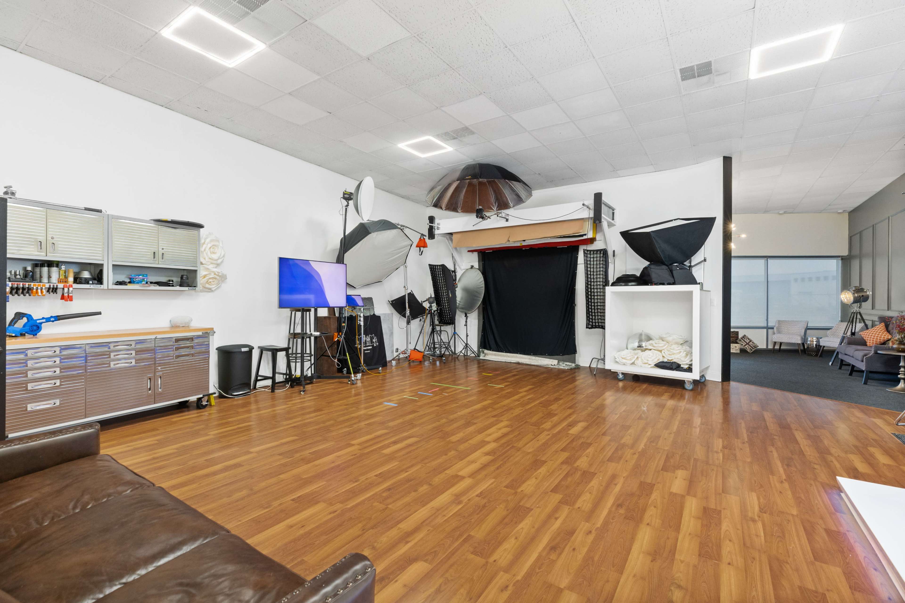 The image shows a spacious photography studio equipped with various lighting equipment, a television, and a comfortable seating area.