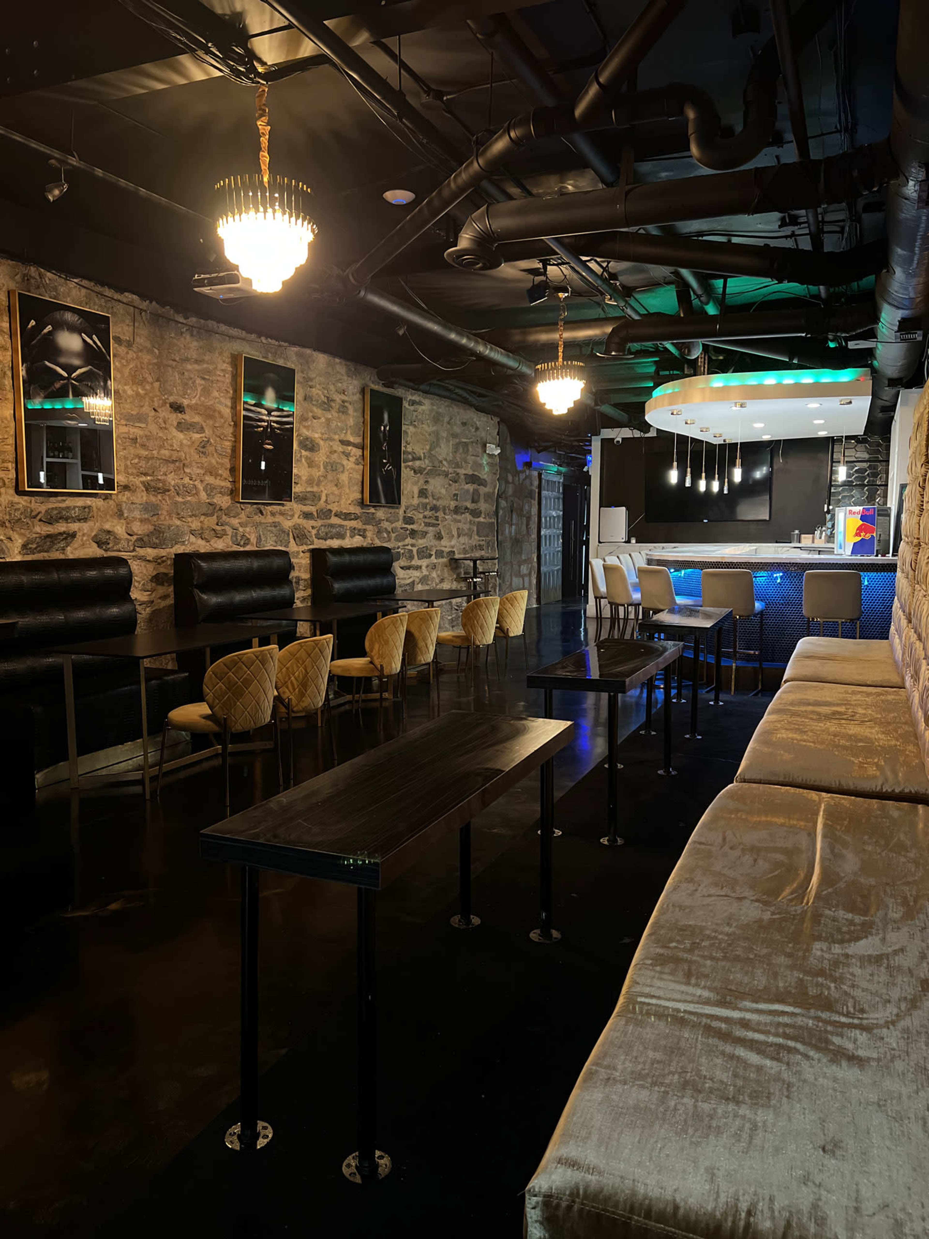 The image shows a dimly lit lounge area with stone walls, plush seating, and elegant lighting fixtures.