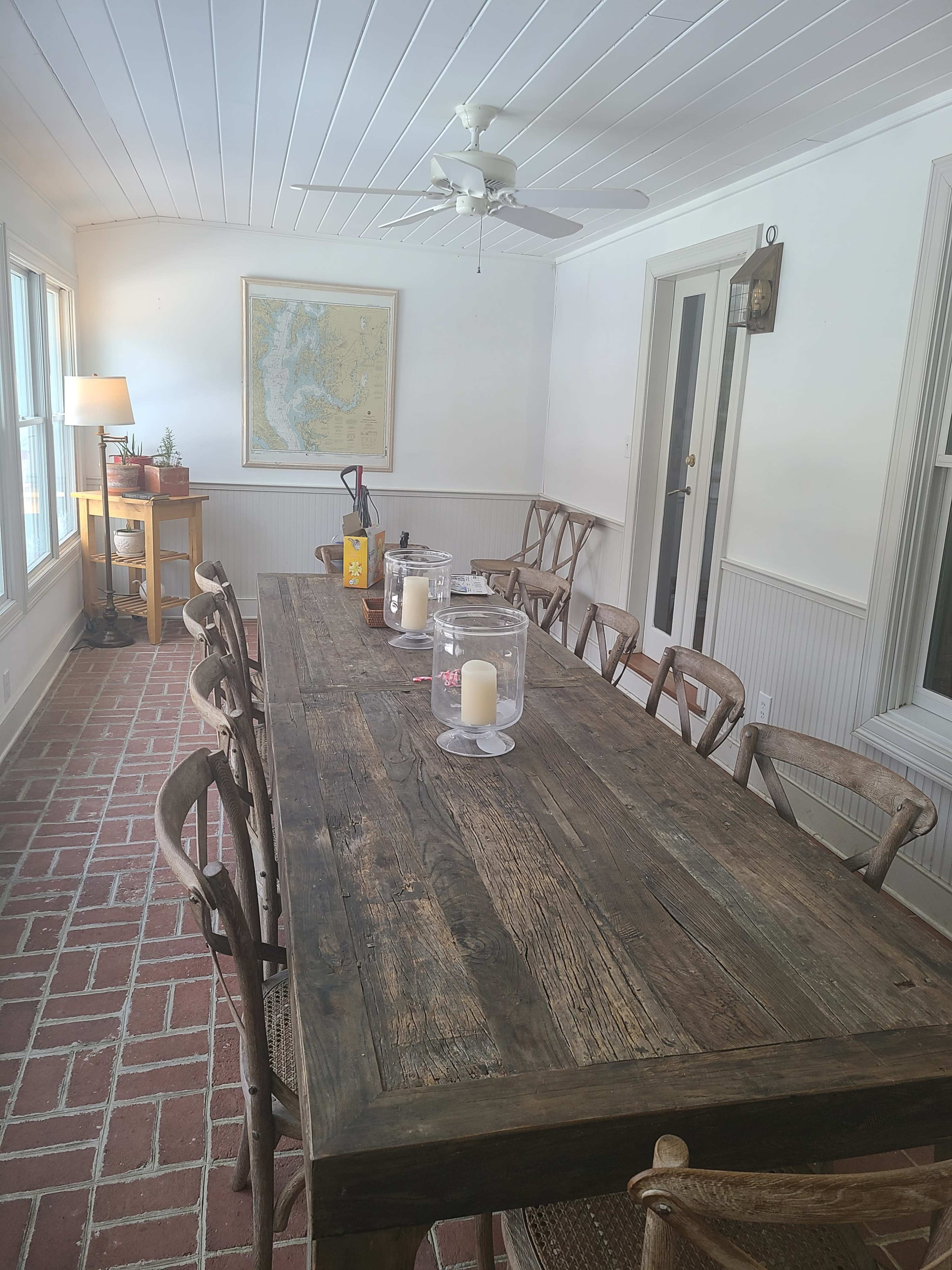 The image shows a spacious dining area with a large wooden table surrounded by chairs, a map on the wall, and a ceiling fan.