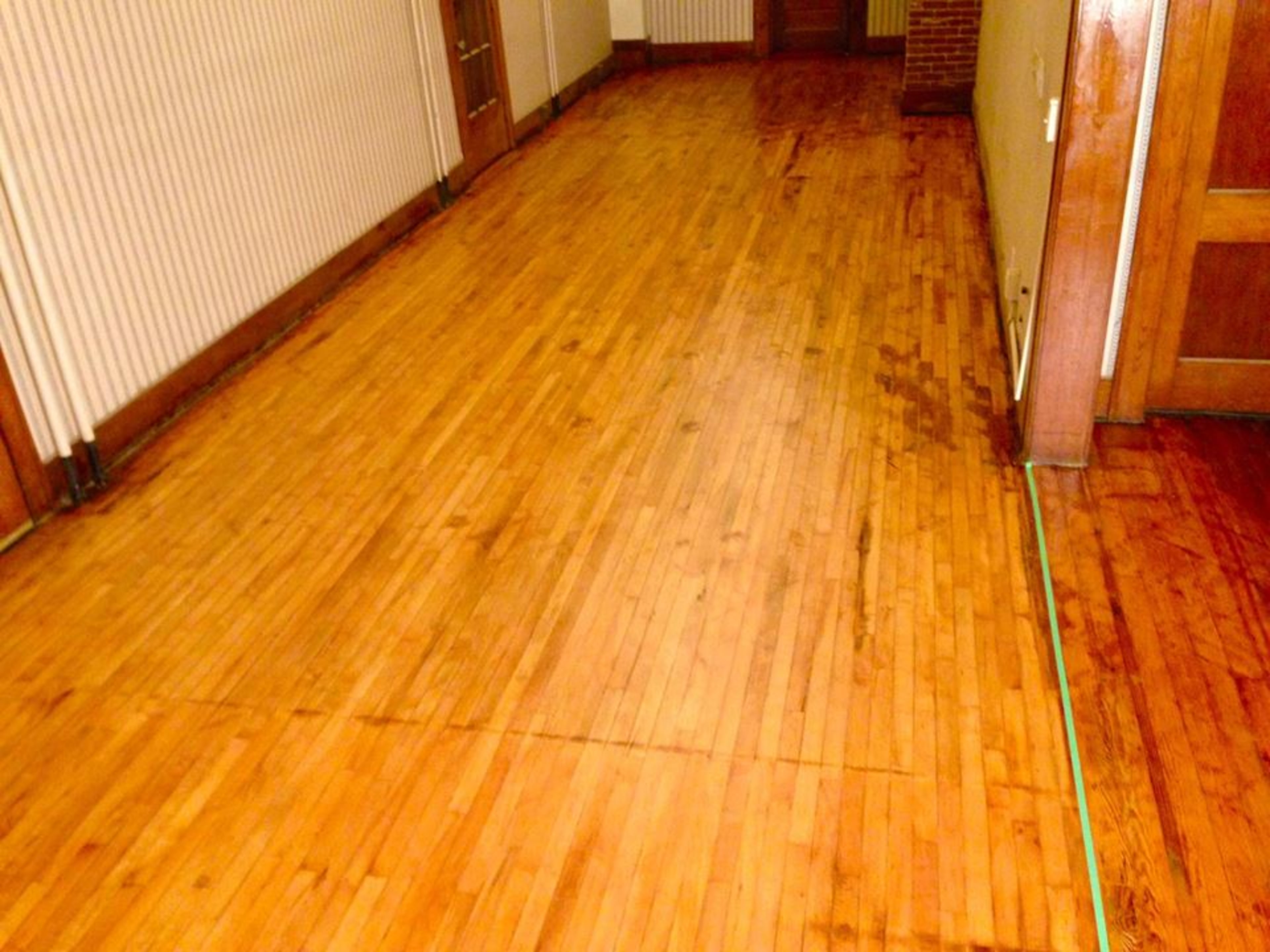 A wooden hallway floor with visible grain patterns and a few darker areas.