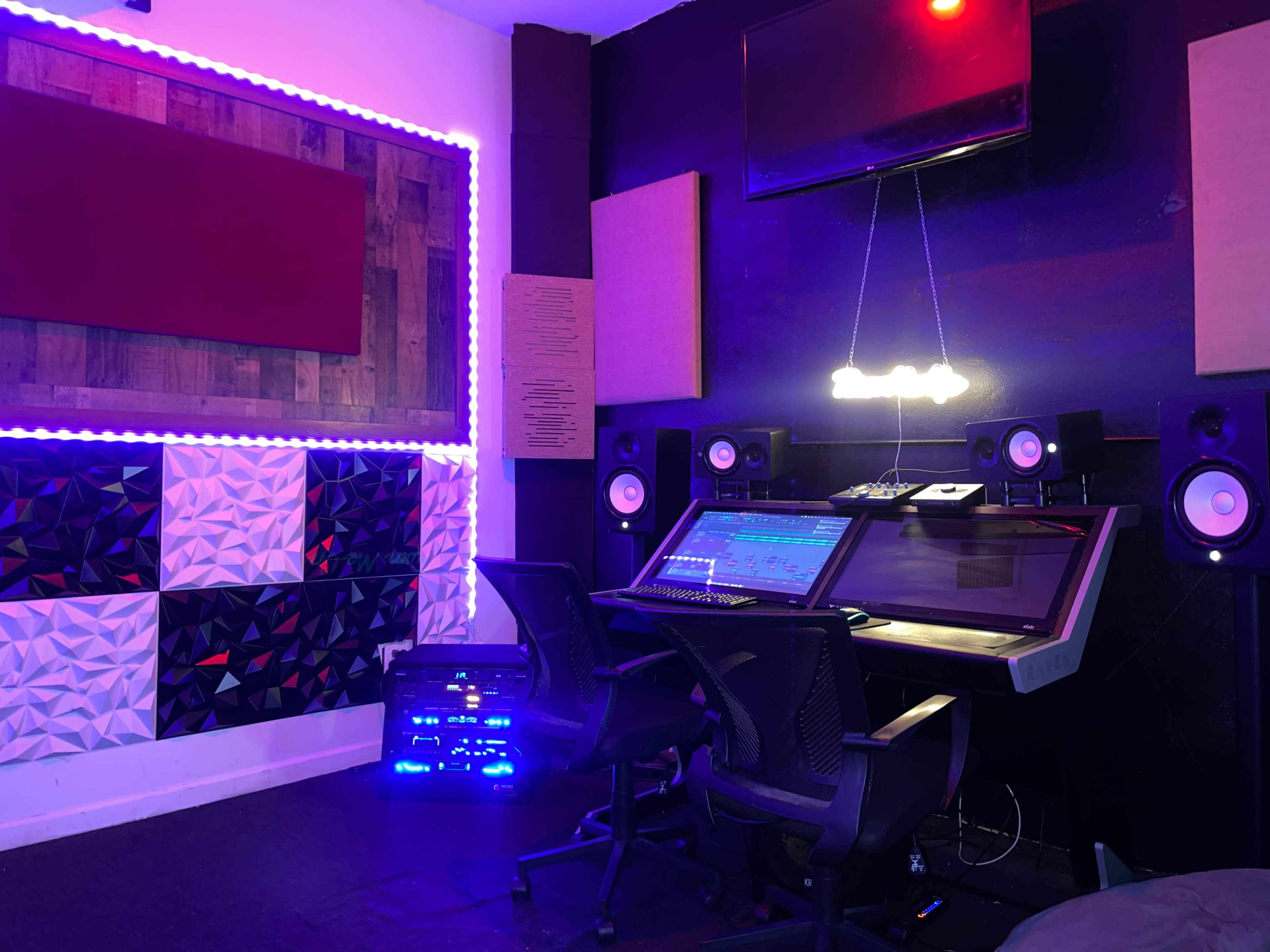 A music production studio featuring a large mixing desk, wall-mounted speakers, and soundproofing panels.