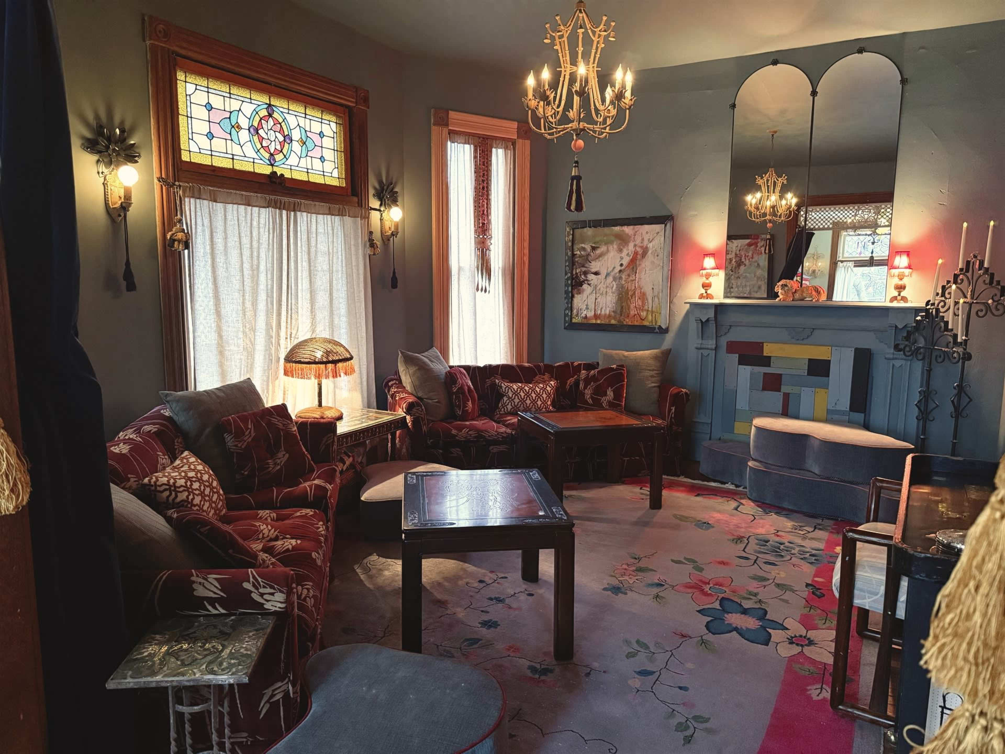 The living room features ornate vintage furnishings, including a velvet sofa set, a decorative lamp, and a colorful rug, all accented by stained glass windows and an ornate fireplace.