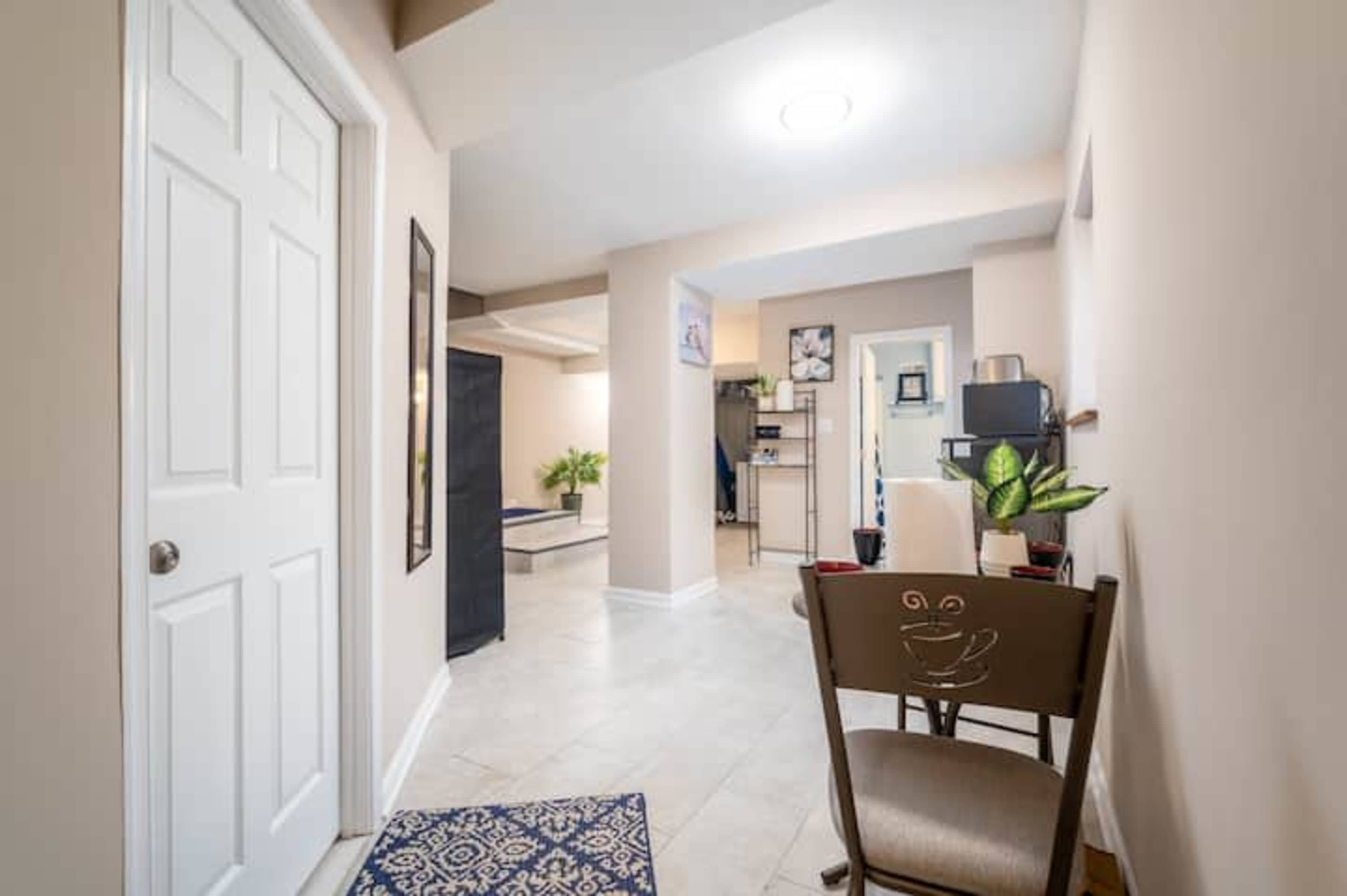 A well-lit hallway leading to a room with a desk and plants, featuring a door on the left and bright walls.