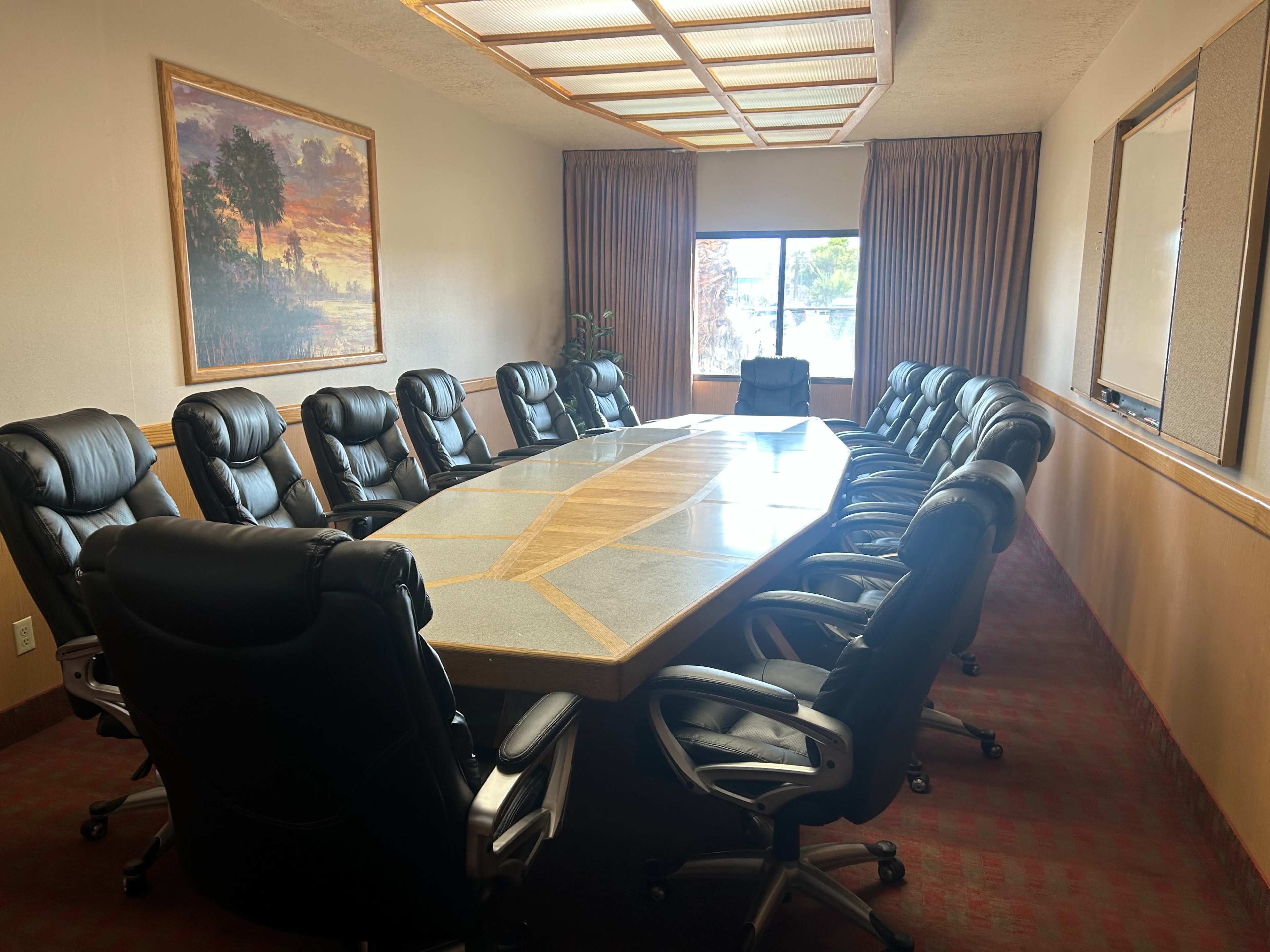 The image shows a large conference room with a long table surrounded by multiple black leather chairs and a window overlooking a view.