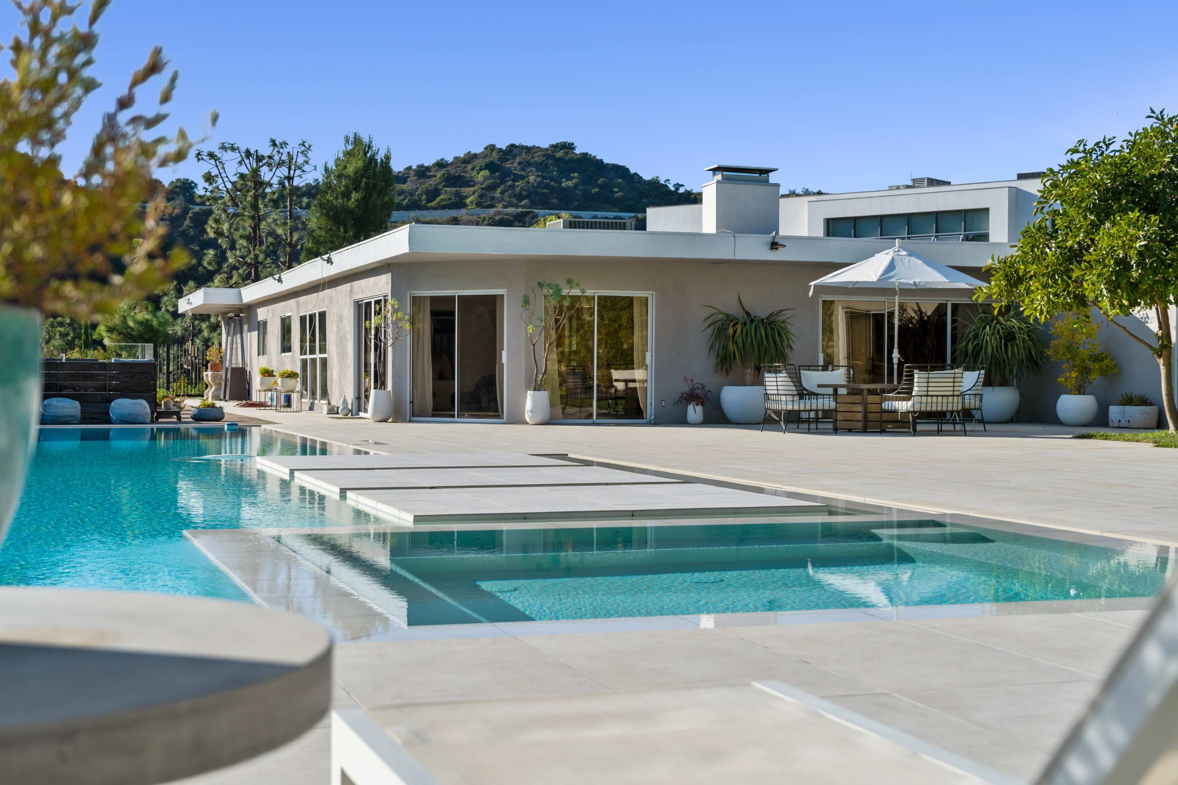 A modern house with large glass windows overlooks a swimming pool and landscaped outdoor area.