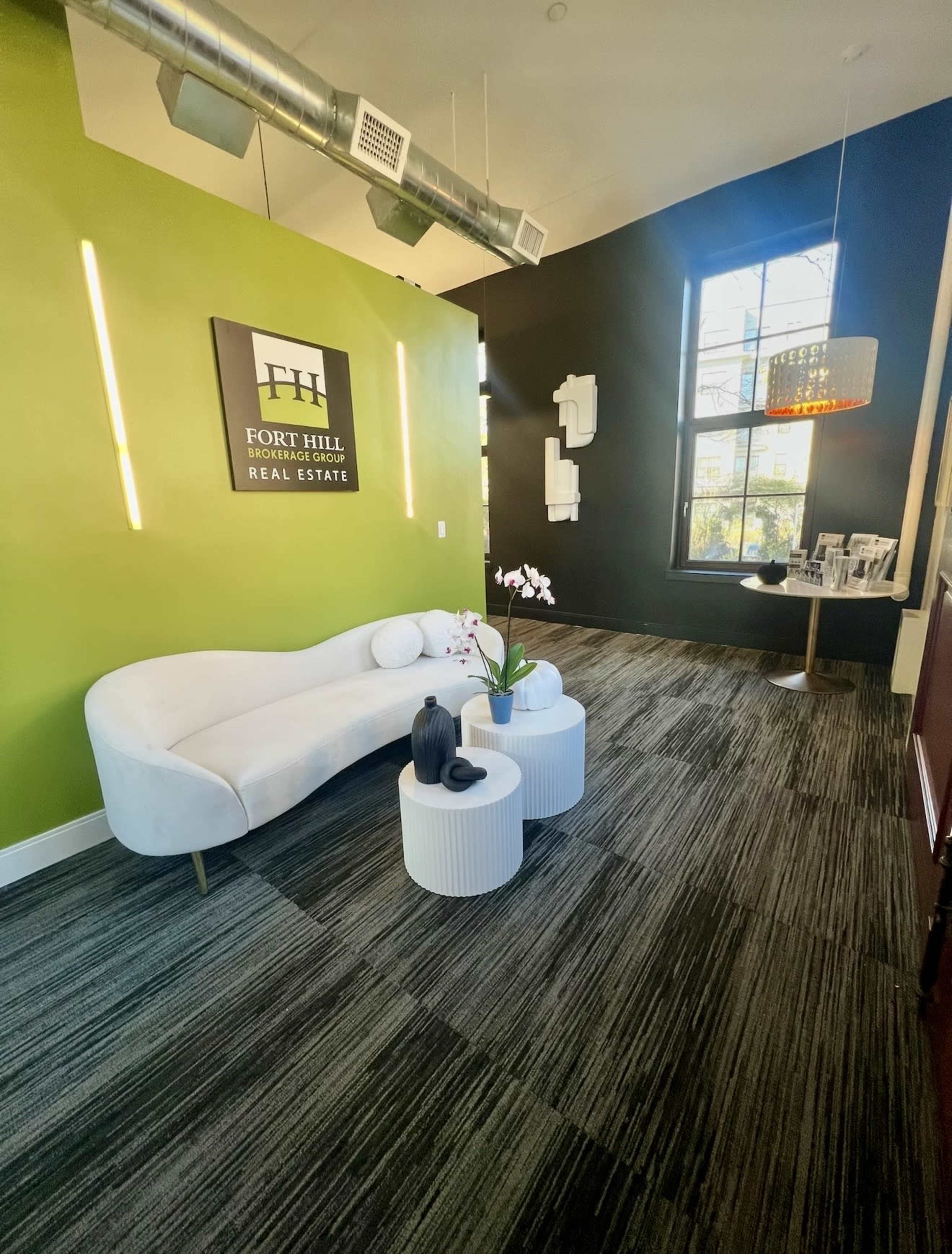 The image shows a modern office reception area with a green and black color scheme, featuring a white couch, two round coffee tables, and decorative elements including plants and artwork.