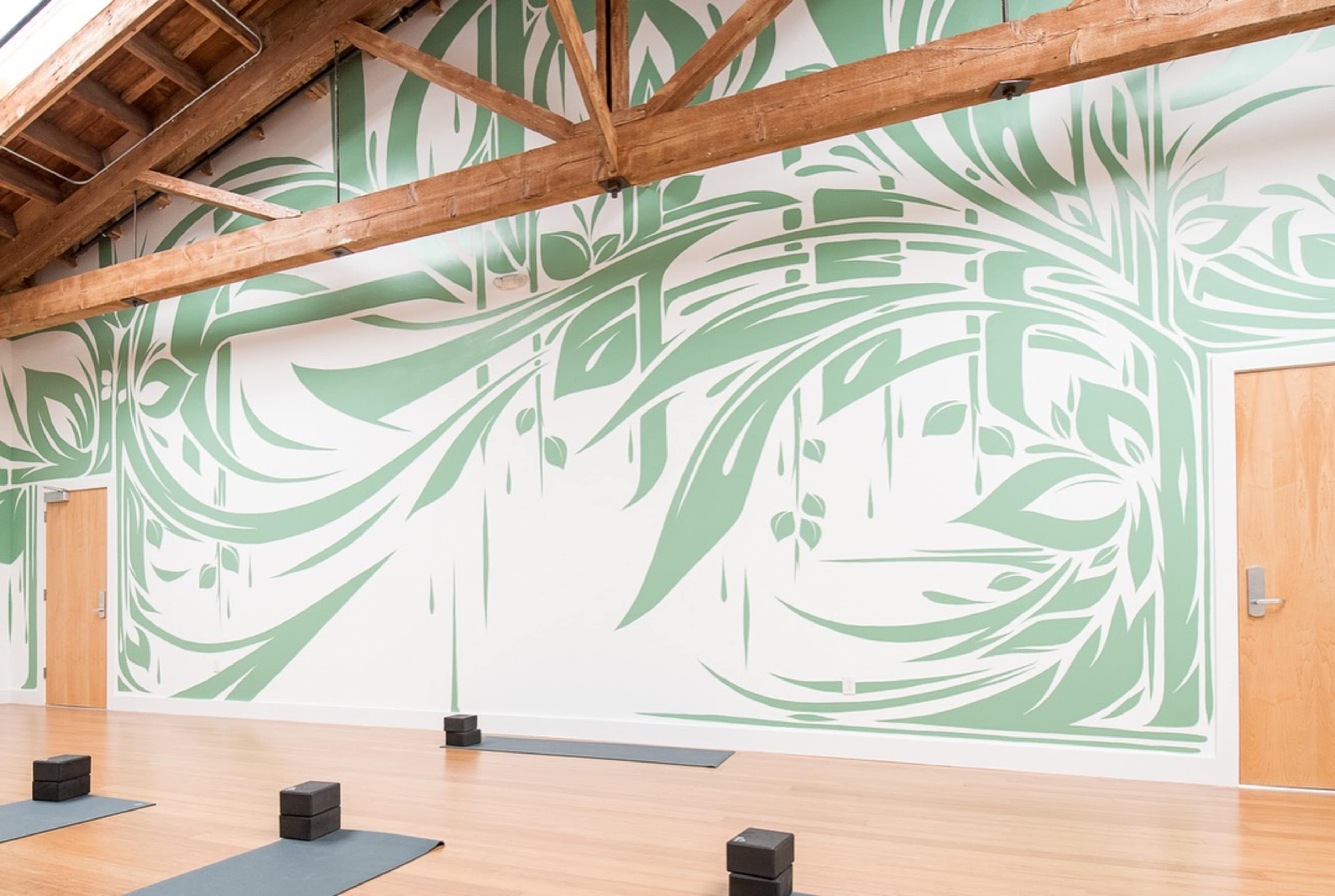 A yoga studio with a large leaf-patterned mural on one wall and black yoga blocks arranged on a wooden floor.