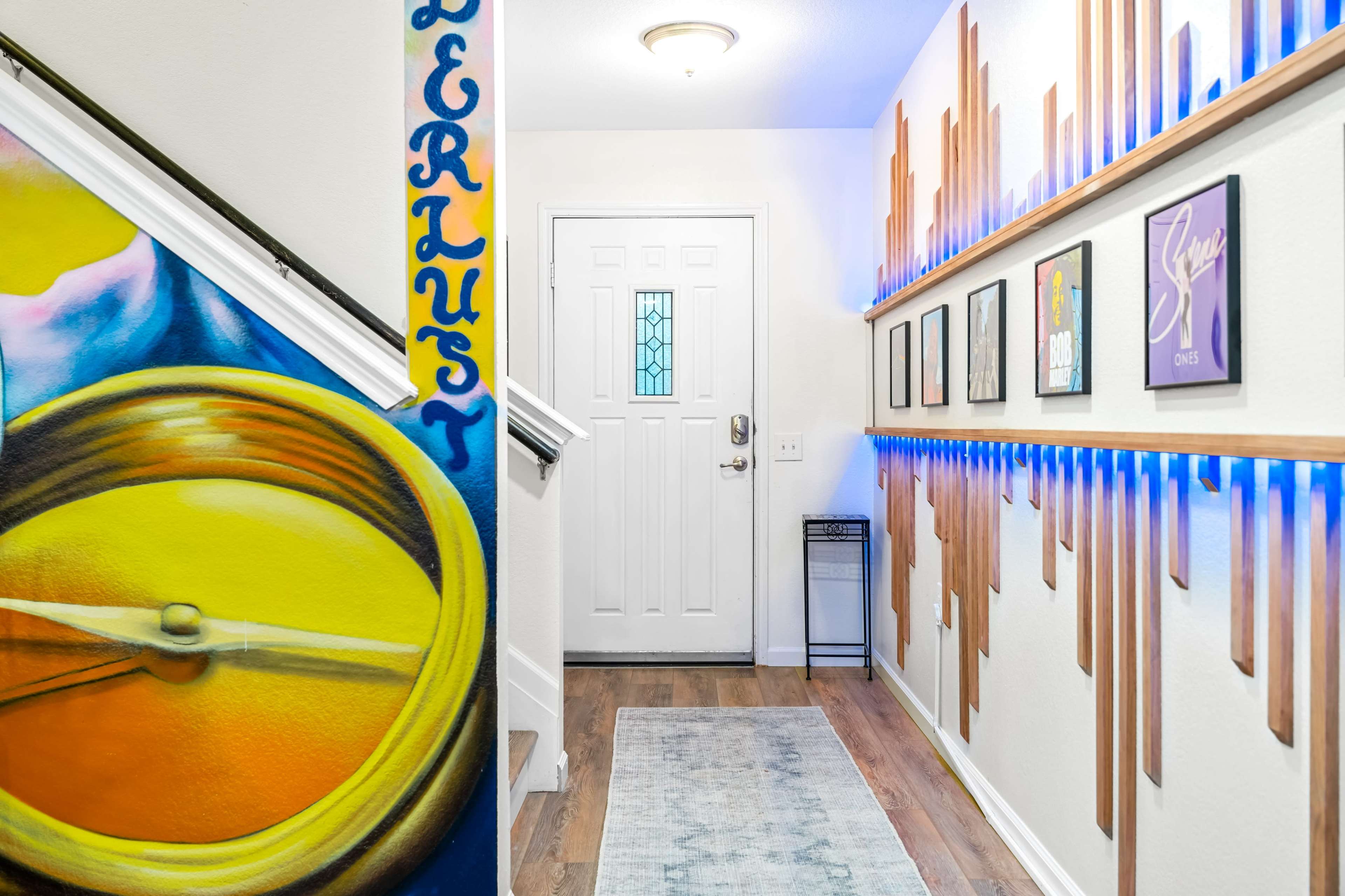A brightly painted hallway featuring a large clock mural on the left and a series of framed pictures along the right wall, complemented by ambient lighting.