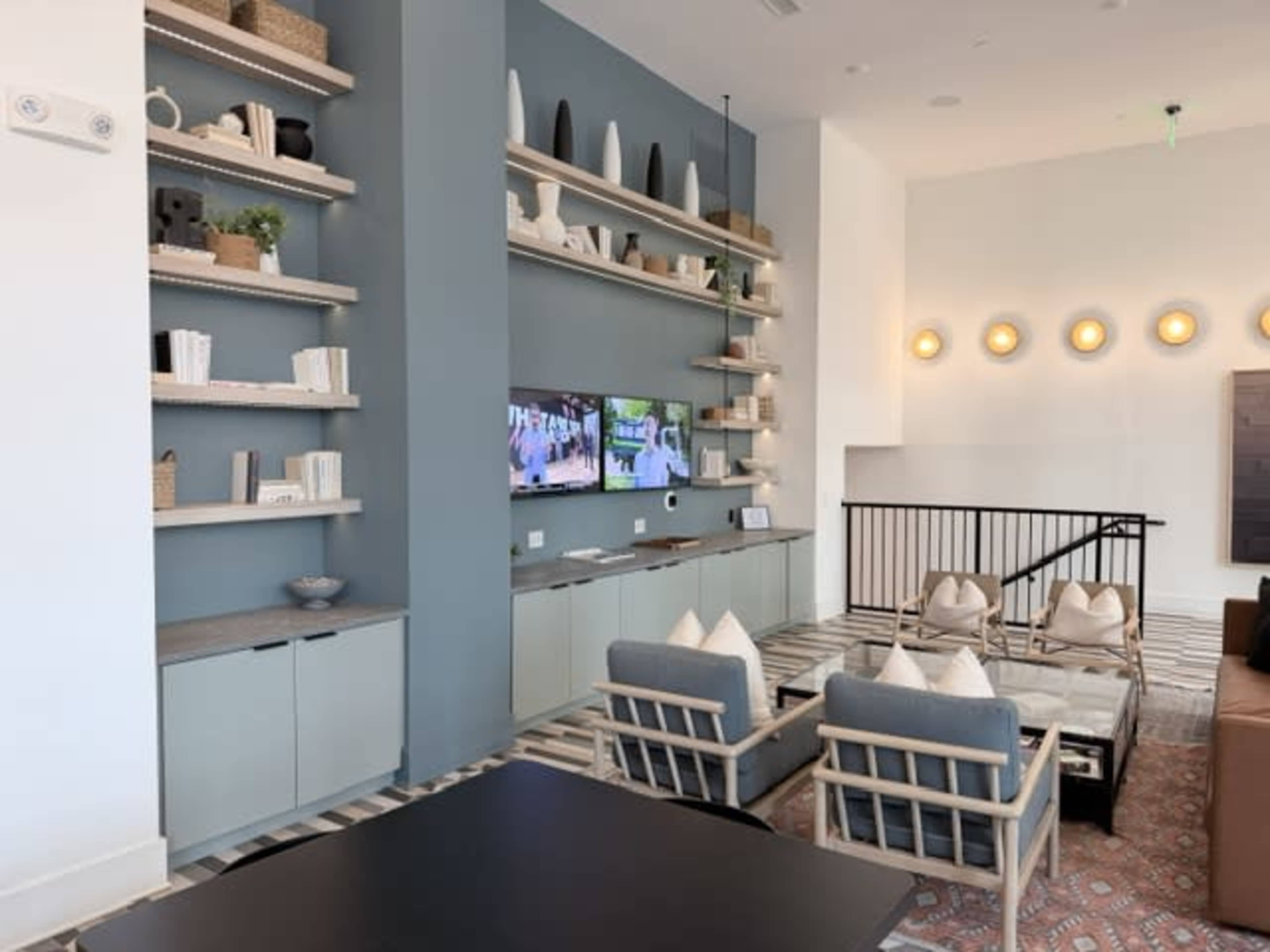 The image shows a modern interior space featuring a light-colored seating area with shelves adorned with decorative objects, a television mounted on a wall, and a patterned floor.