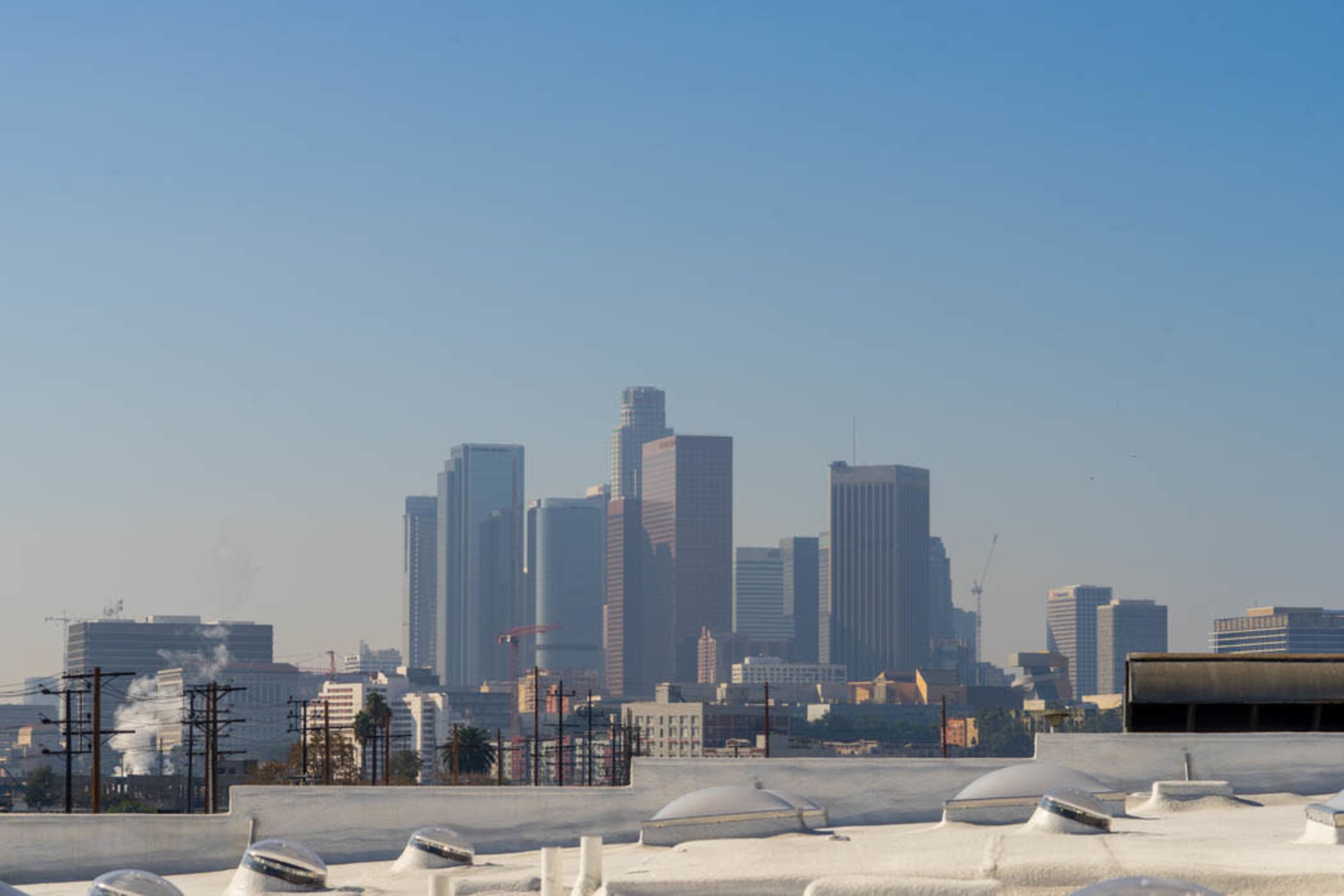 The image shows the skyline of downtown Los Angeles with modern skyscrapers against a clear blue sky.