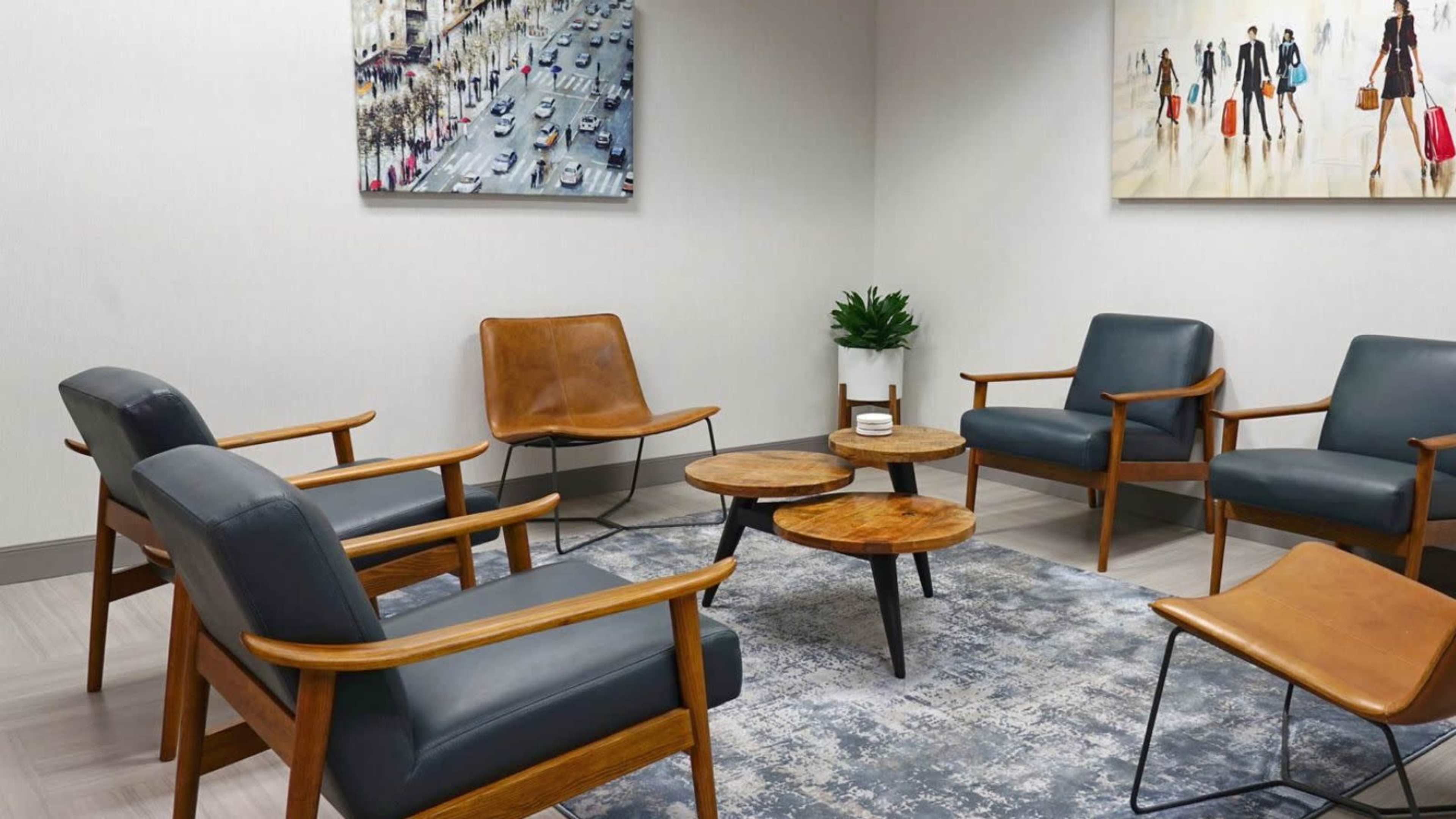 A modern waiting area with four chairs, a circular wooden coffee table, and a decorative plant, all arranged around a patterned rug.