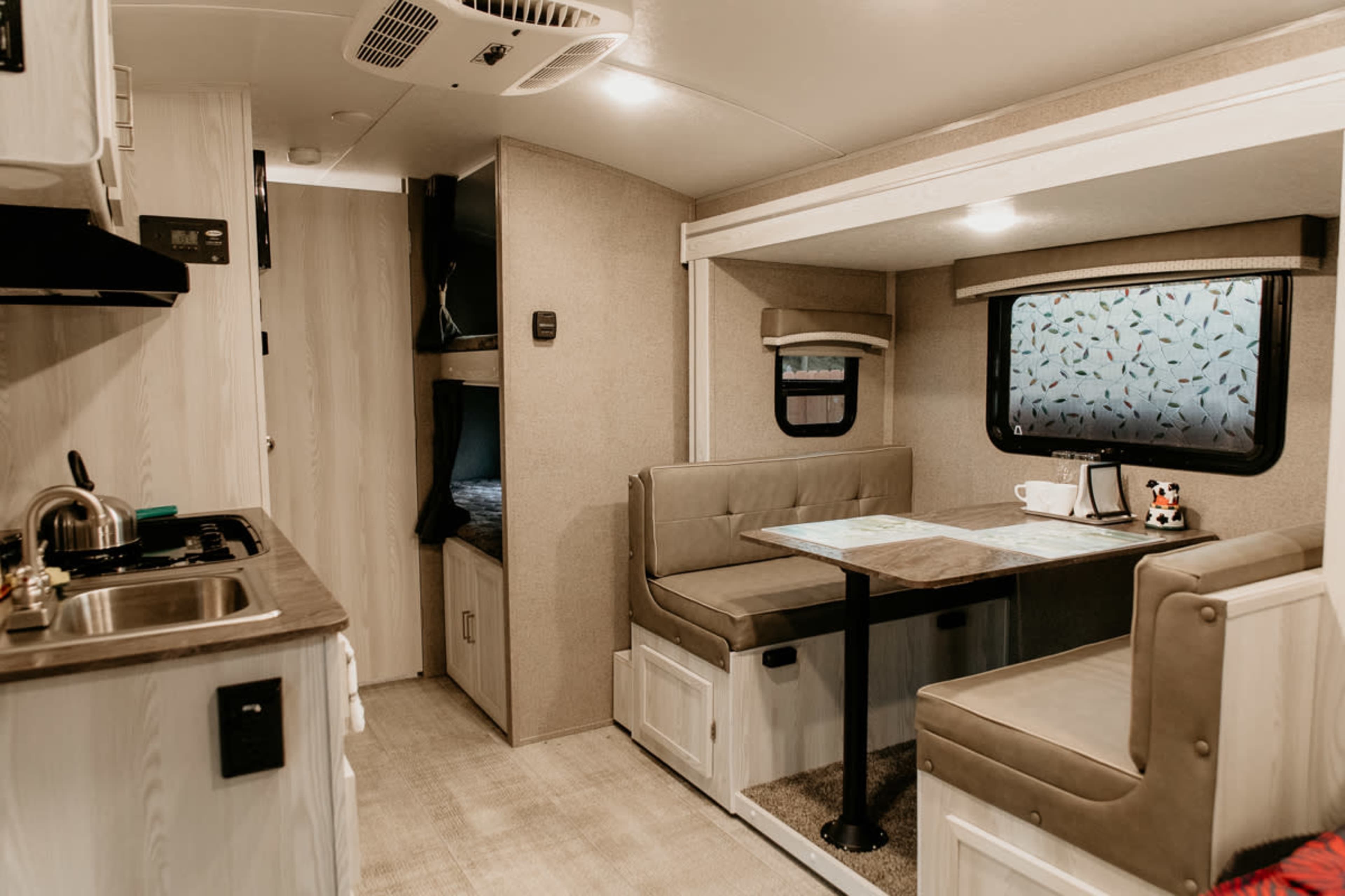 The interior of a small RV, featuring a dining area with a table and bench seating, a kitchenette with a sink, and storage cabinets.