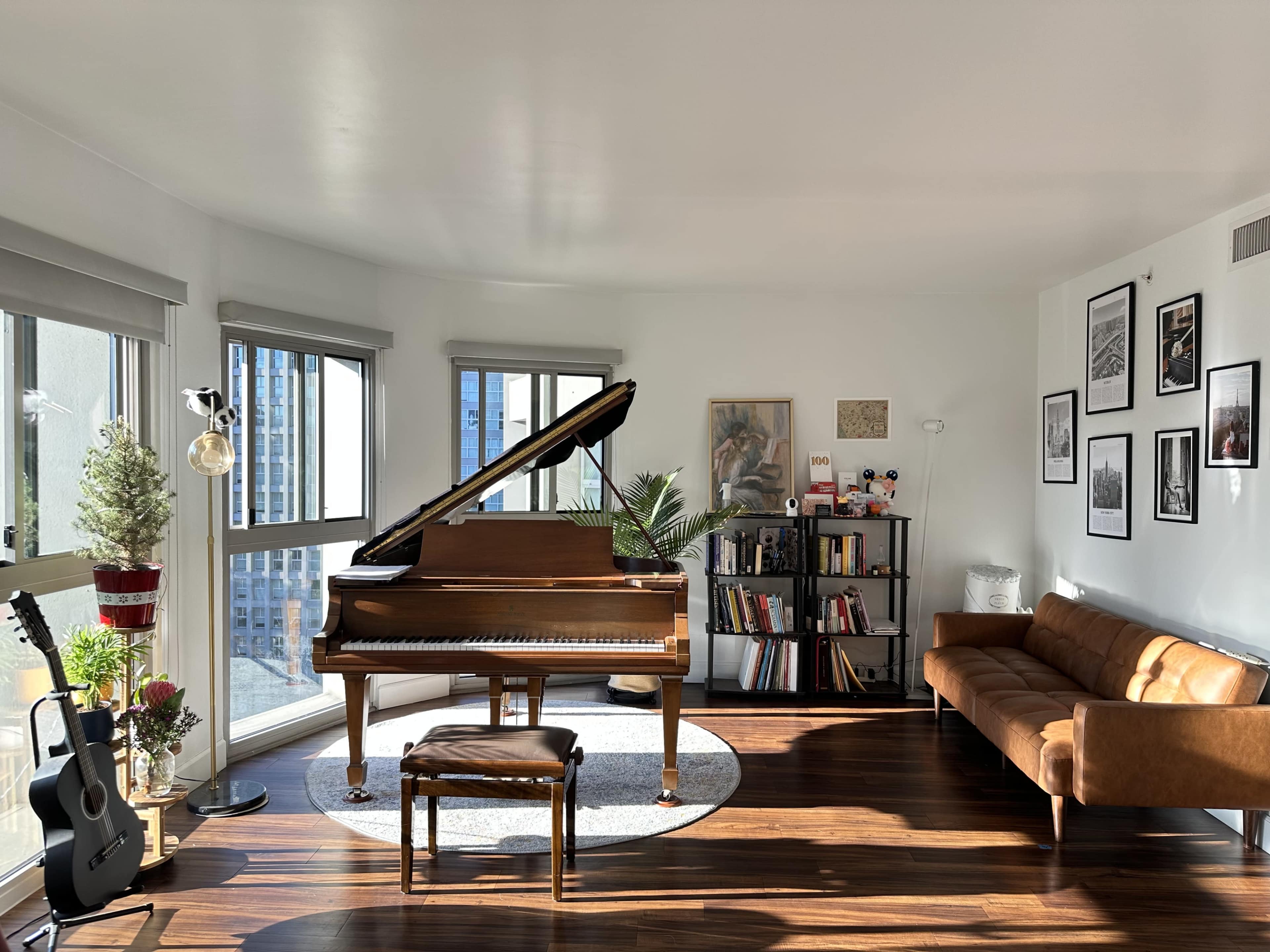 A grand piano sits prominently in a sunlit corner of a modern living room adorned with bookshelves, a comfortable couch, and various decorative elements.