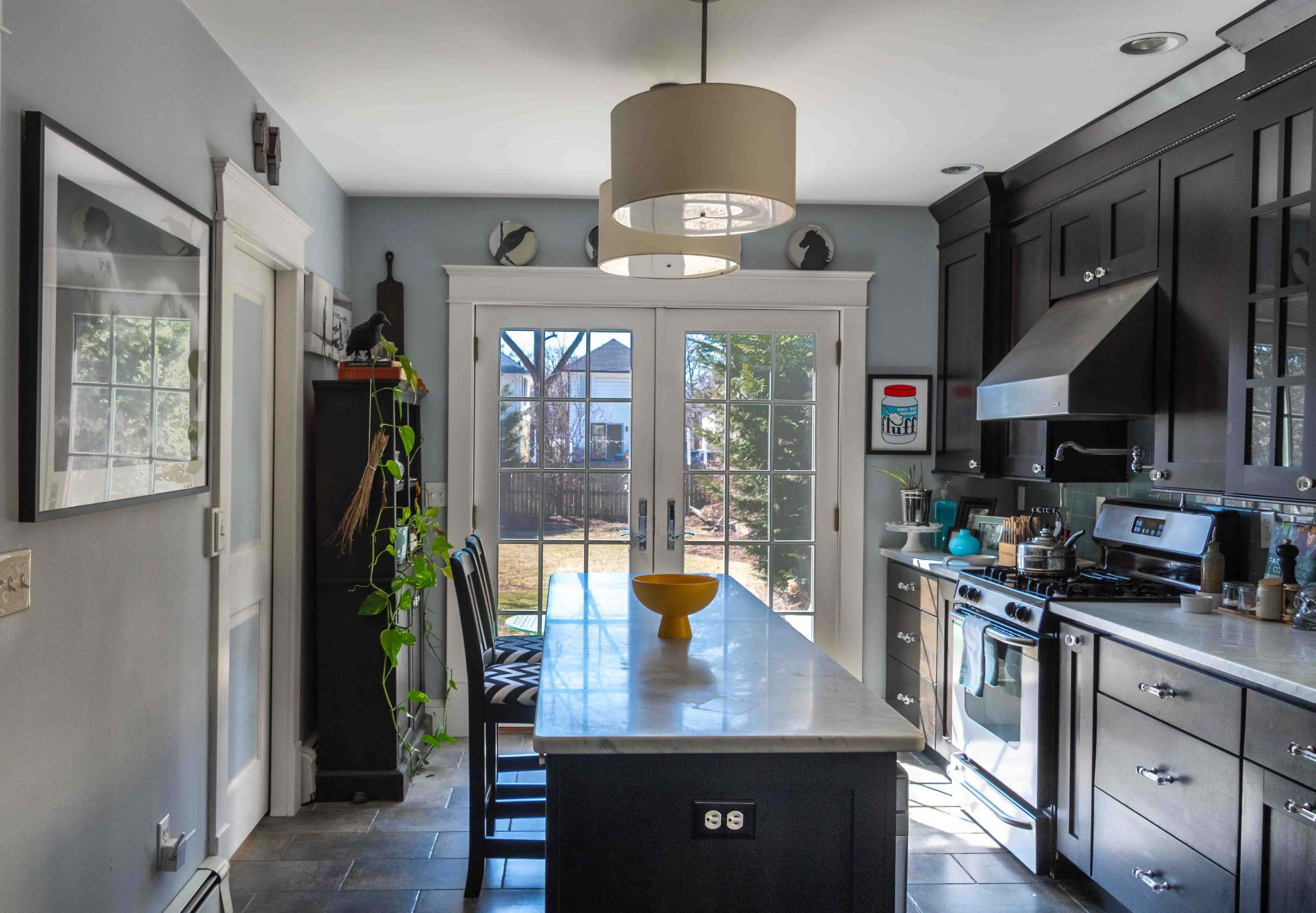 The kitchen features a large marble island with a yellow bowl, dark cabinetry, and doors leading to a backyard.