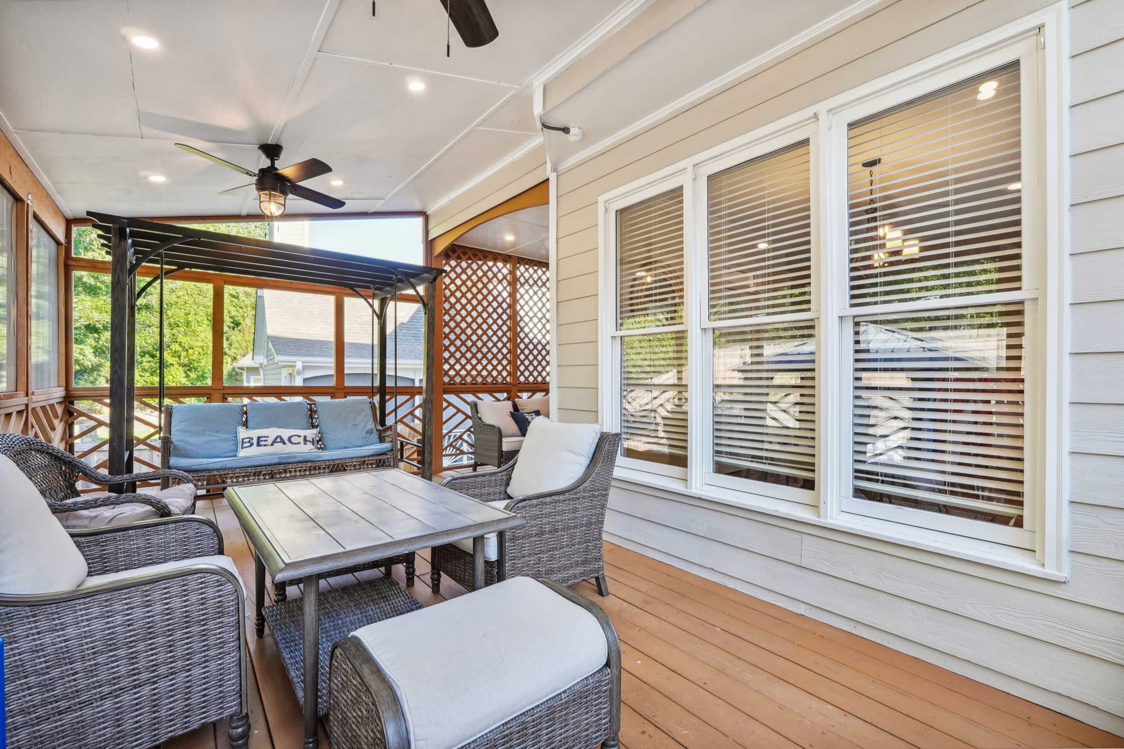 A covered outdoor seating area with wicker furniture and a view of a nearby garden.