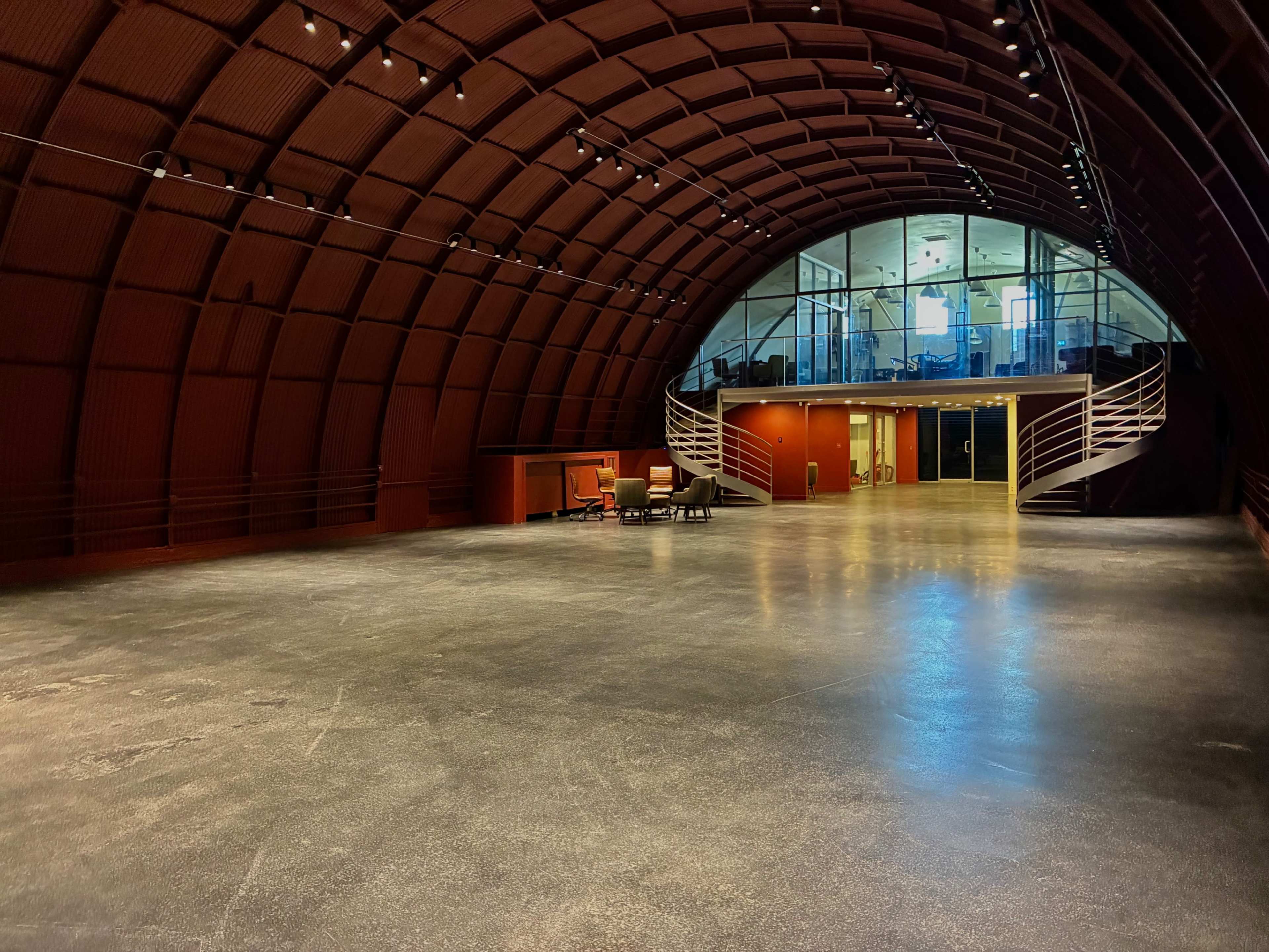 The image shows an empty, large, modern interior space with a curved red ceiling and a glass-walled area in the background.