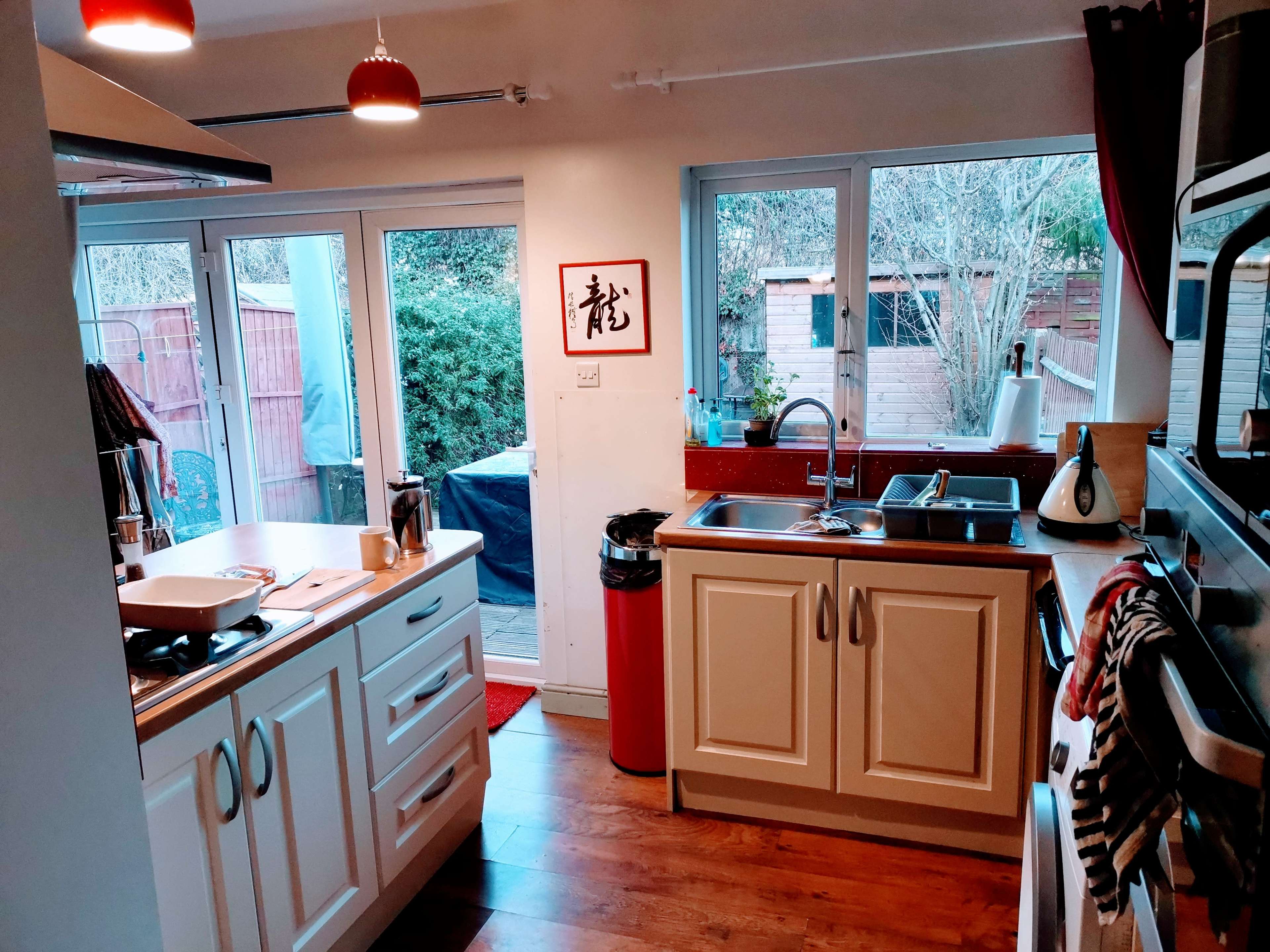 A modern kitchen with white cabinets, a sink, and large windows overlooking a backyard.
