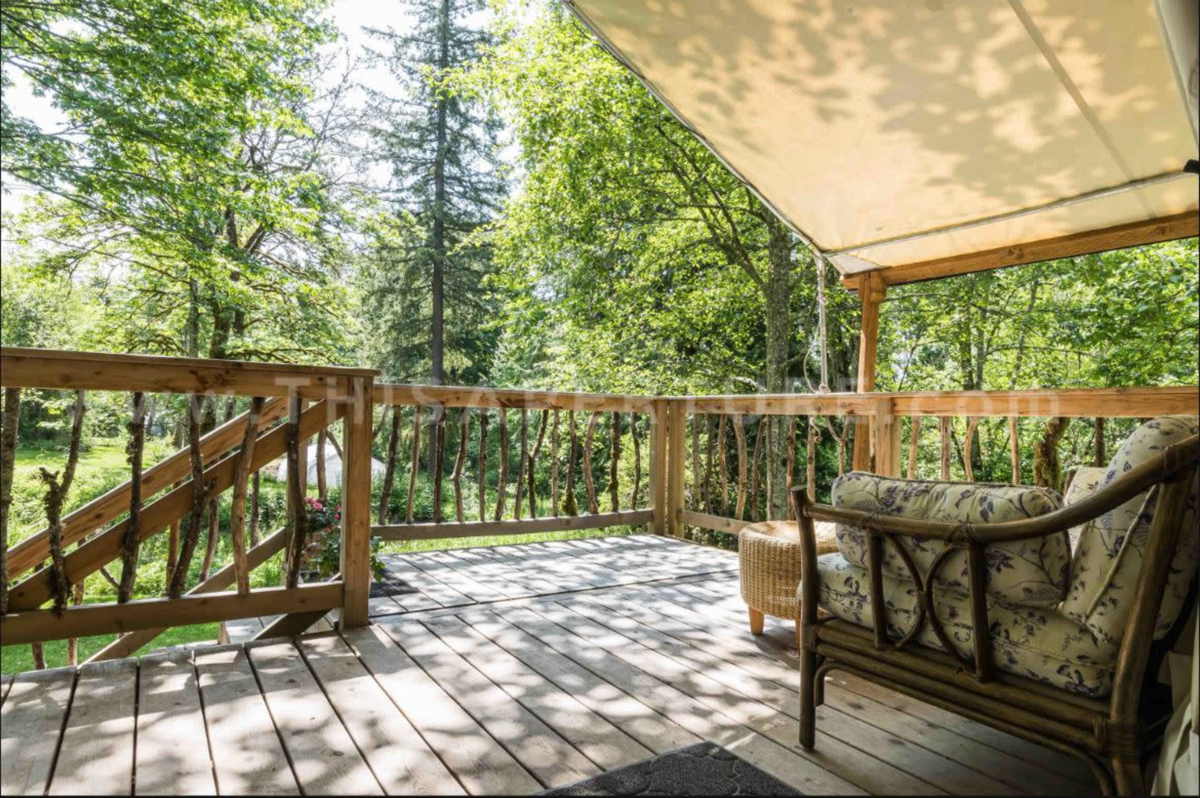 A wooden deck with a comfortable chair overlooks a green forested area.