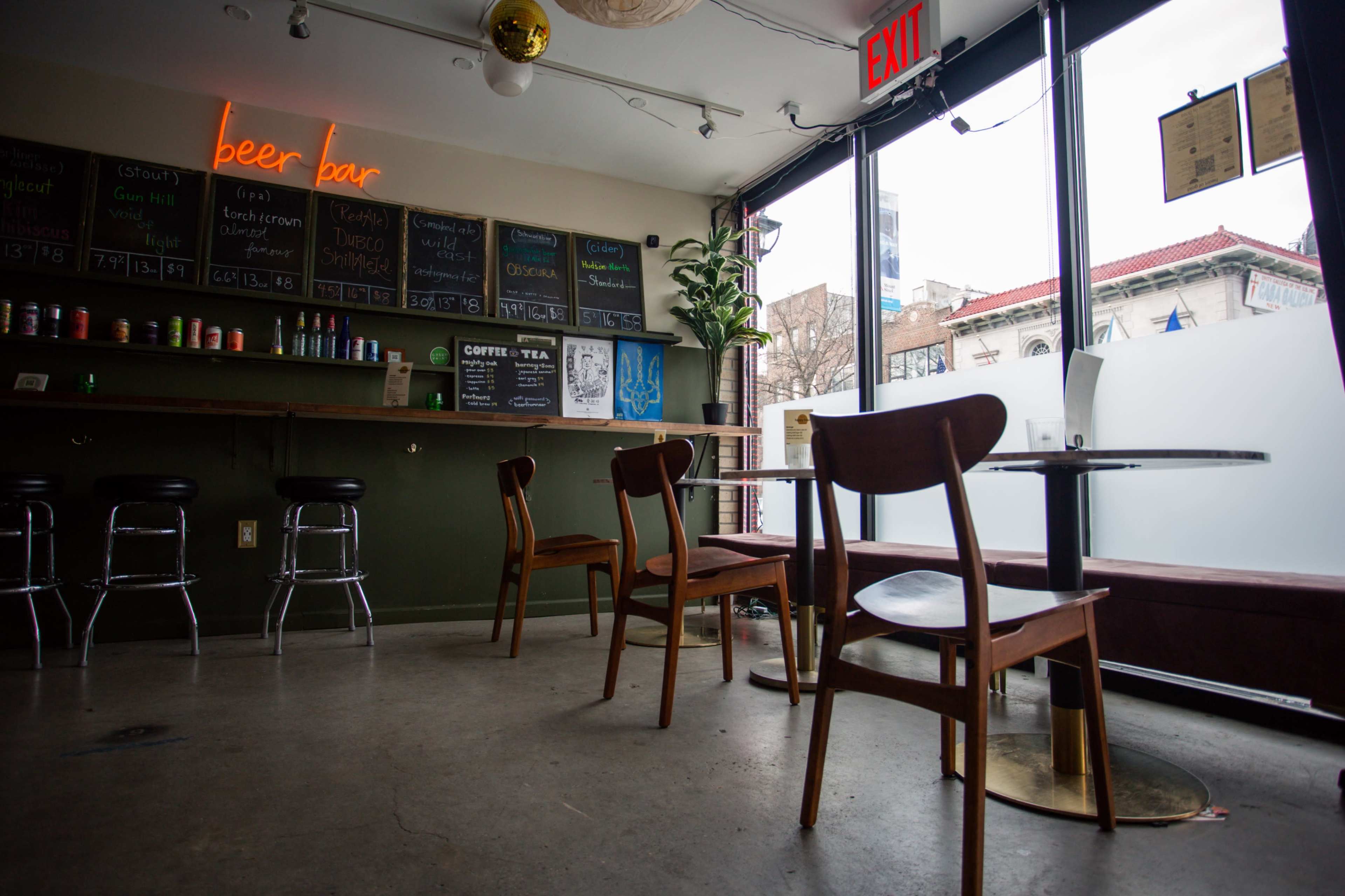 A modern coffee and beer bar with a simple interior featuring wooden chairs, a green bar counter, and a menu board on the wall.