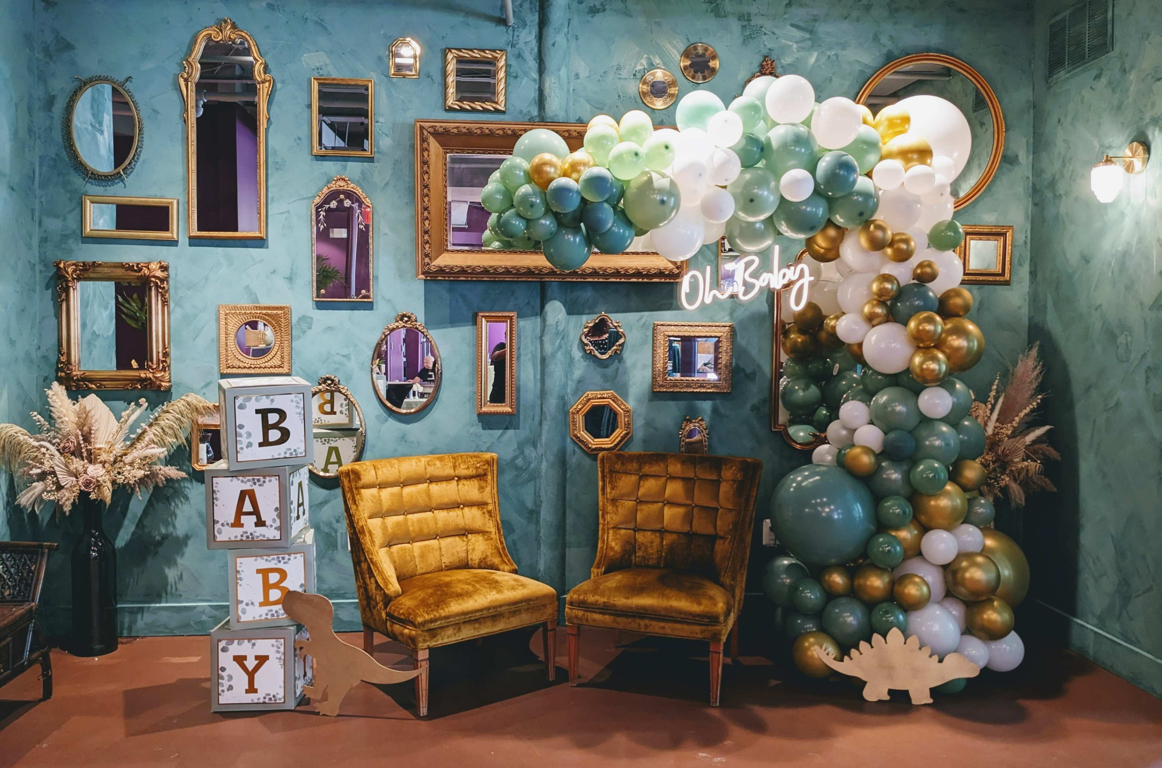A decorated room with a balloon arch, vintage mirrors on the walls, and two yellow chairs beside decorated blocks that spell out "BABY."
