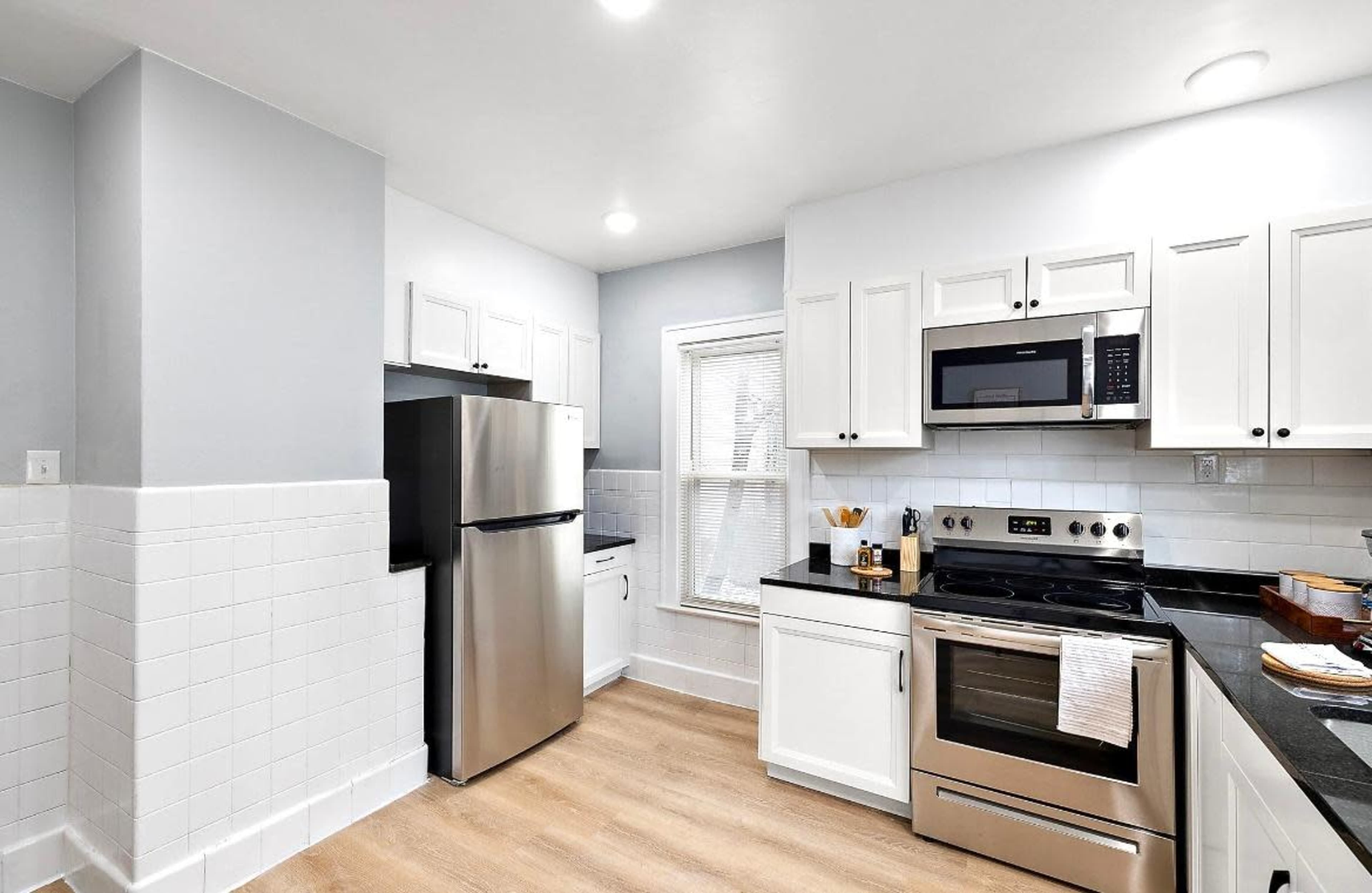 A modern kitchen features stainless steel appliances, white cabinetry, and a light-colored laminate floor.