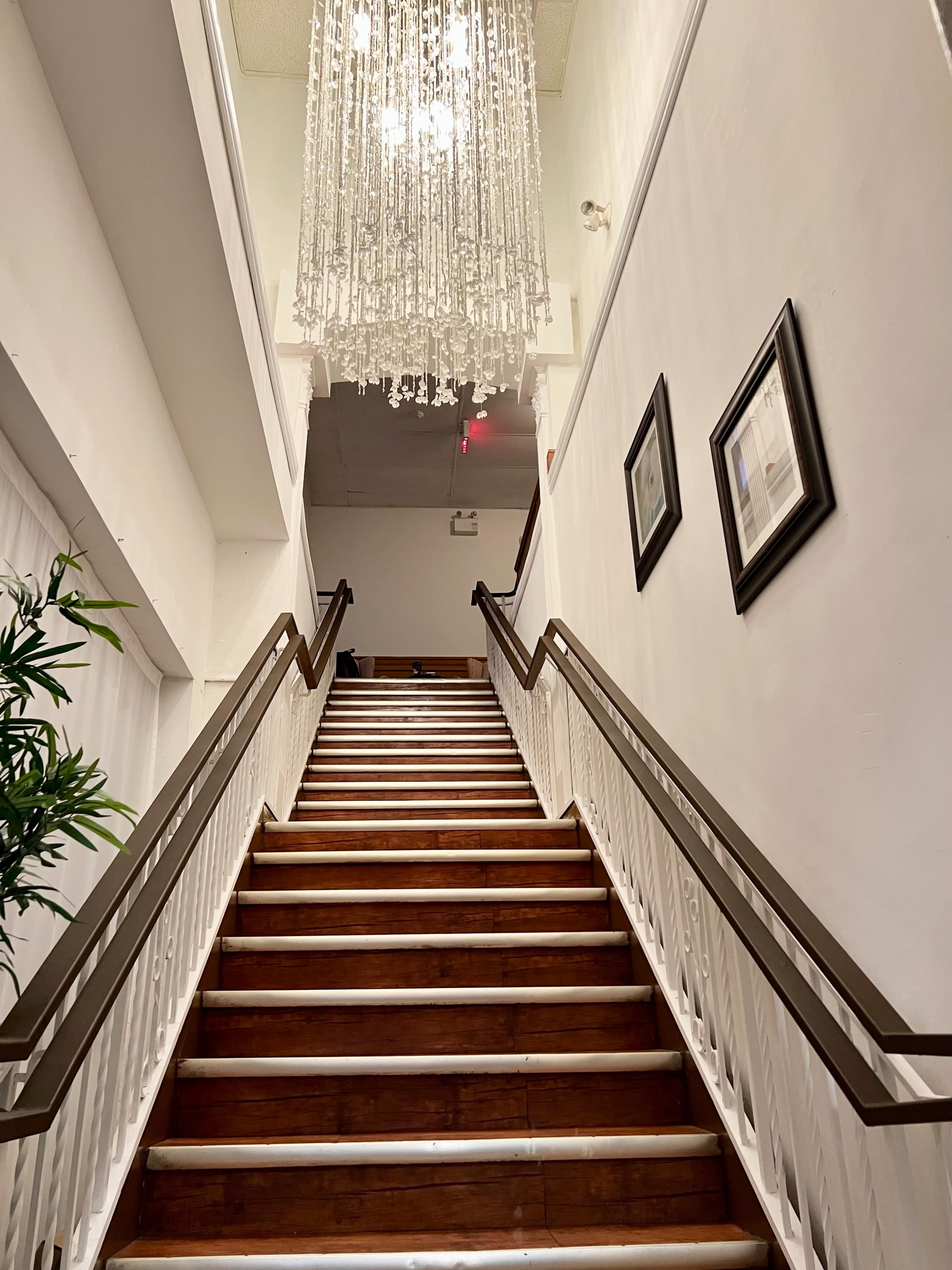 A staircase with wooden steps and a white banister leads up to a chandelier hanging from the ceiling.