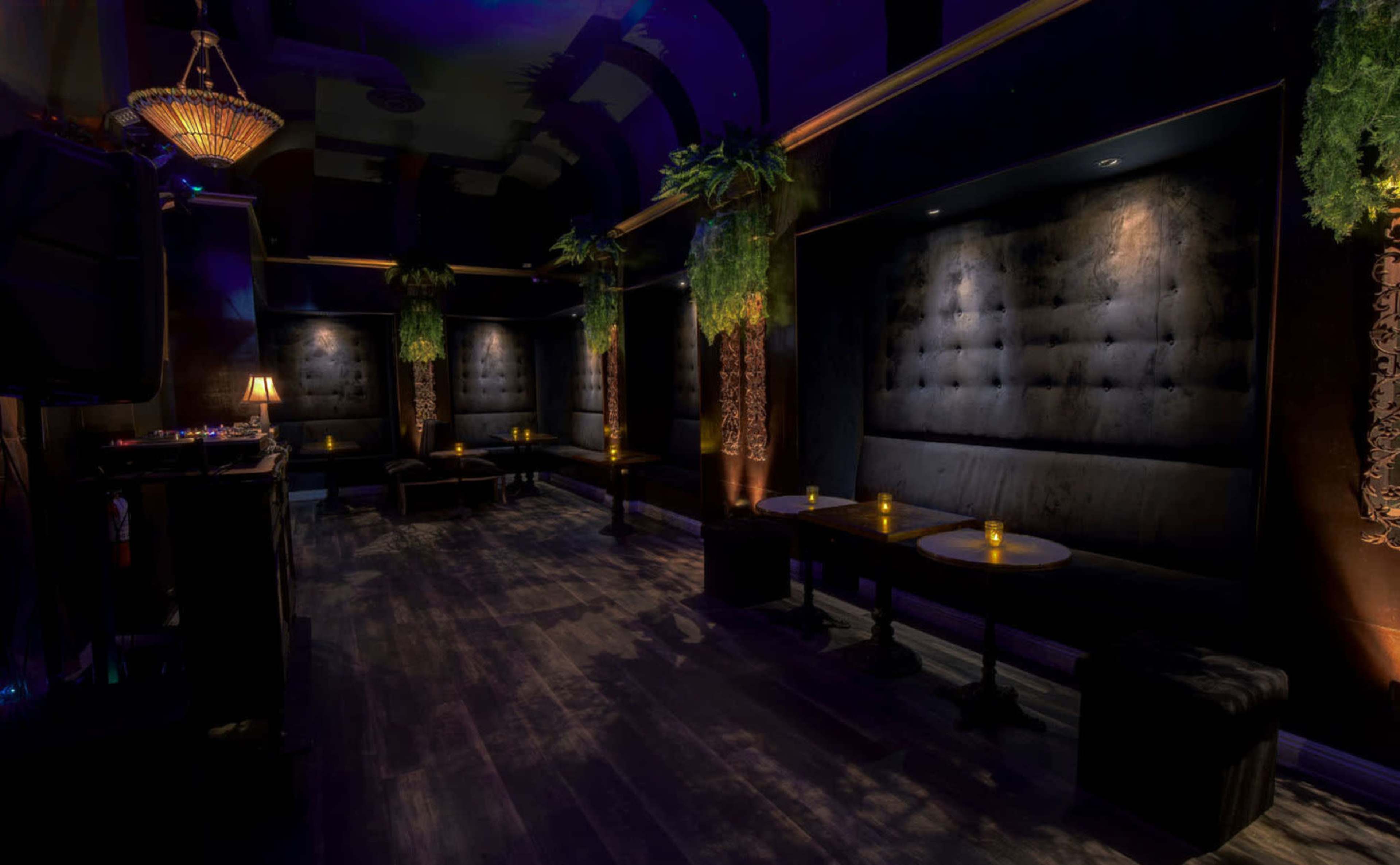 The image shows an empty upscale lounge with dark decor, plush seating along the walls, and soft lighting from small table candles.