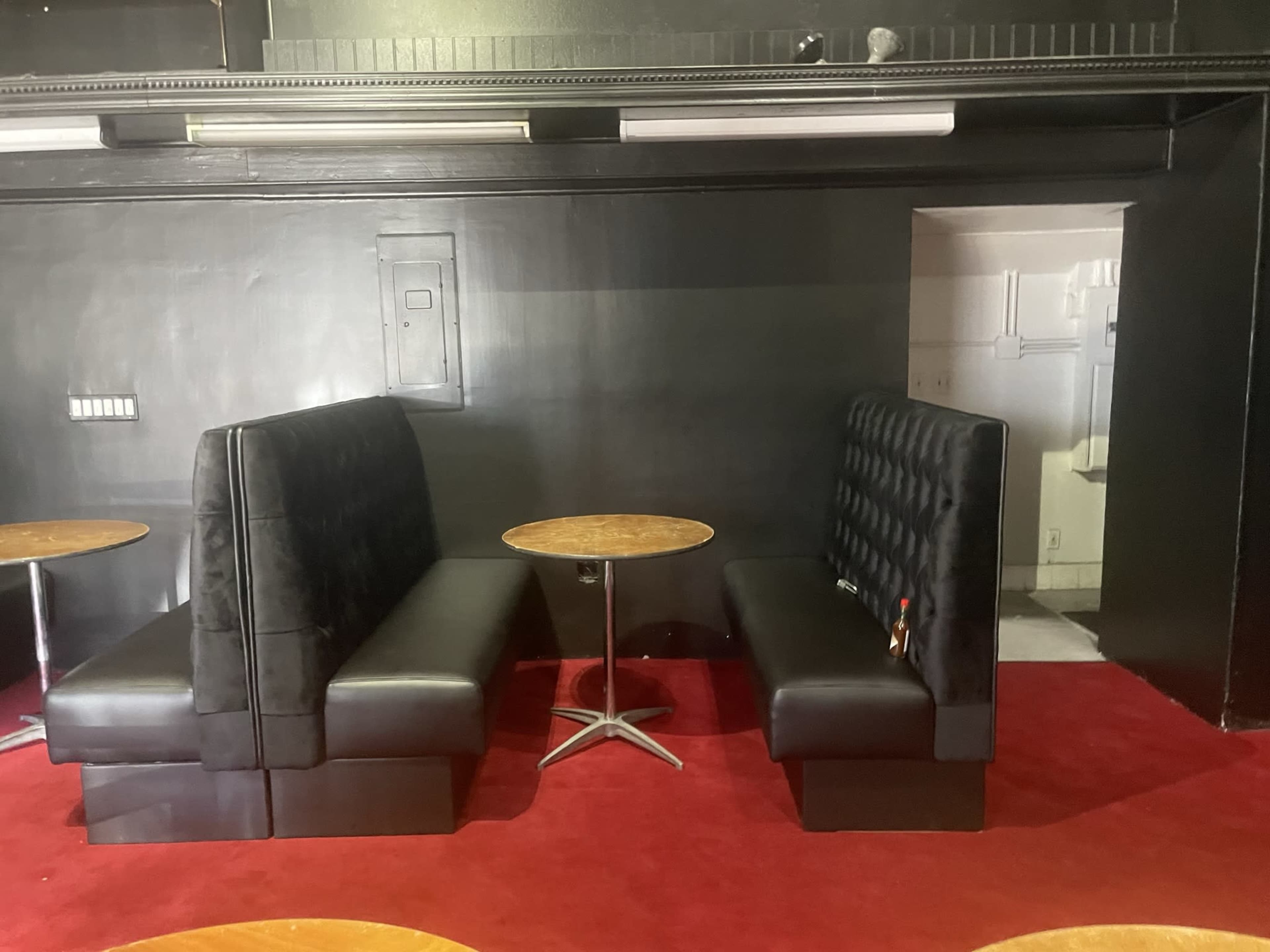 Two black leather booth seats facing each other across a small round table, set on red carpet in a dimly lit room.