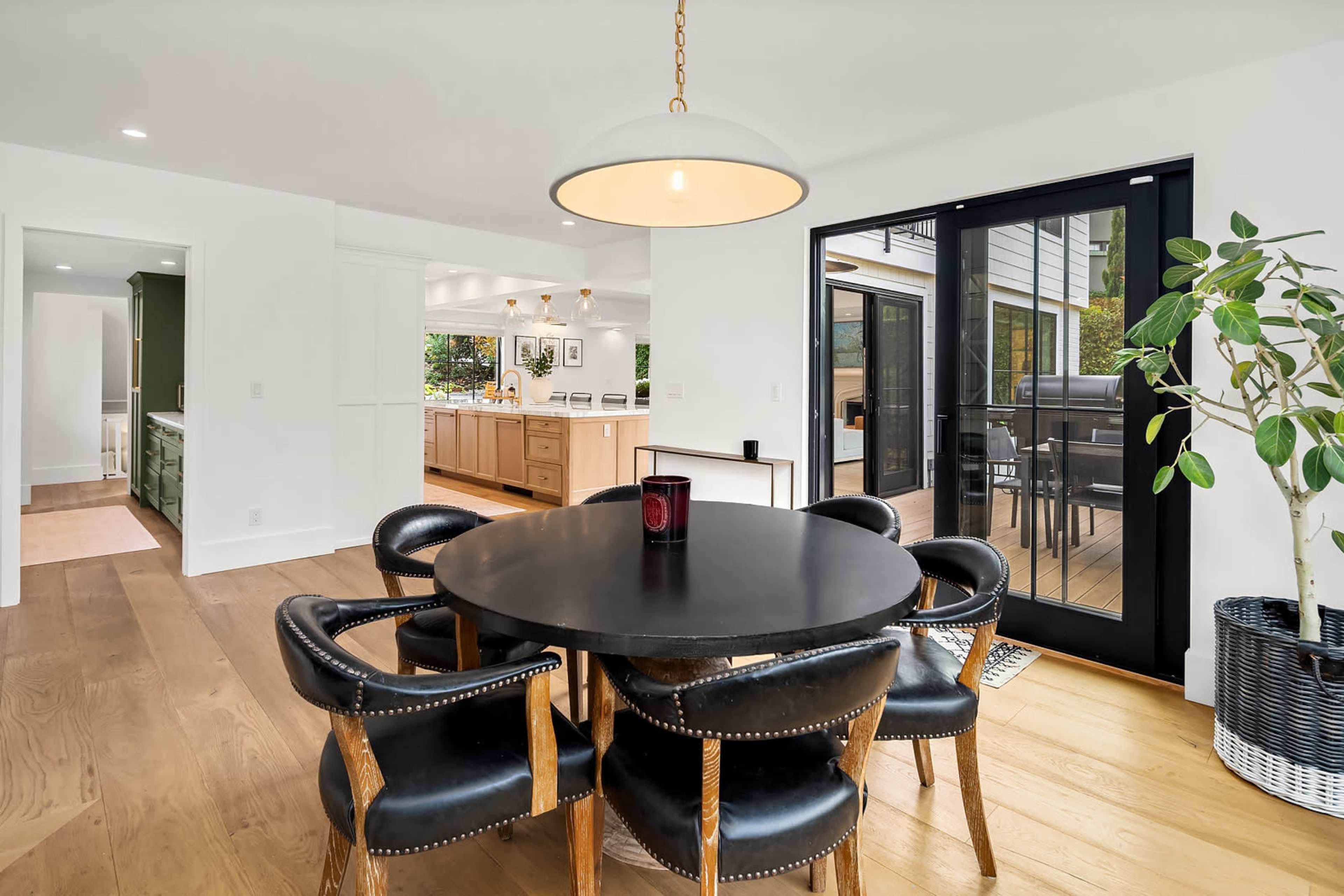 A round black dining table with four chairs is set in a bright kitchen area that opens to a deck through glass doors.