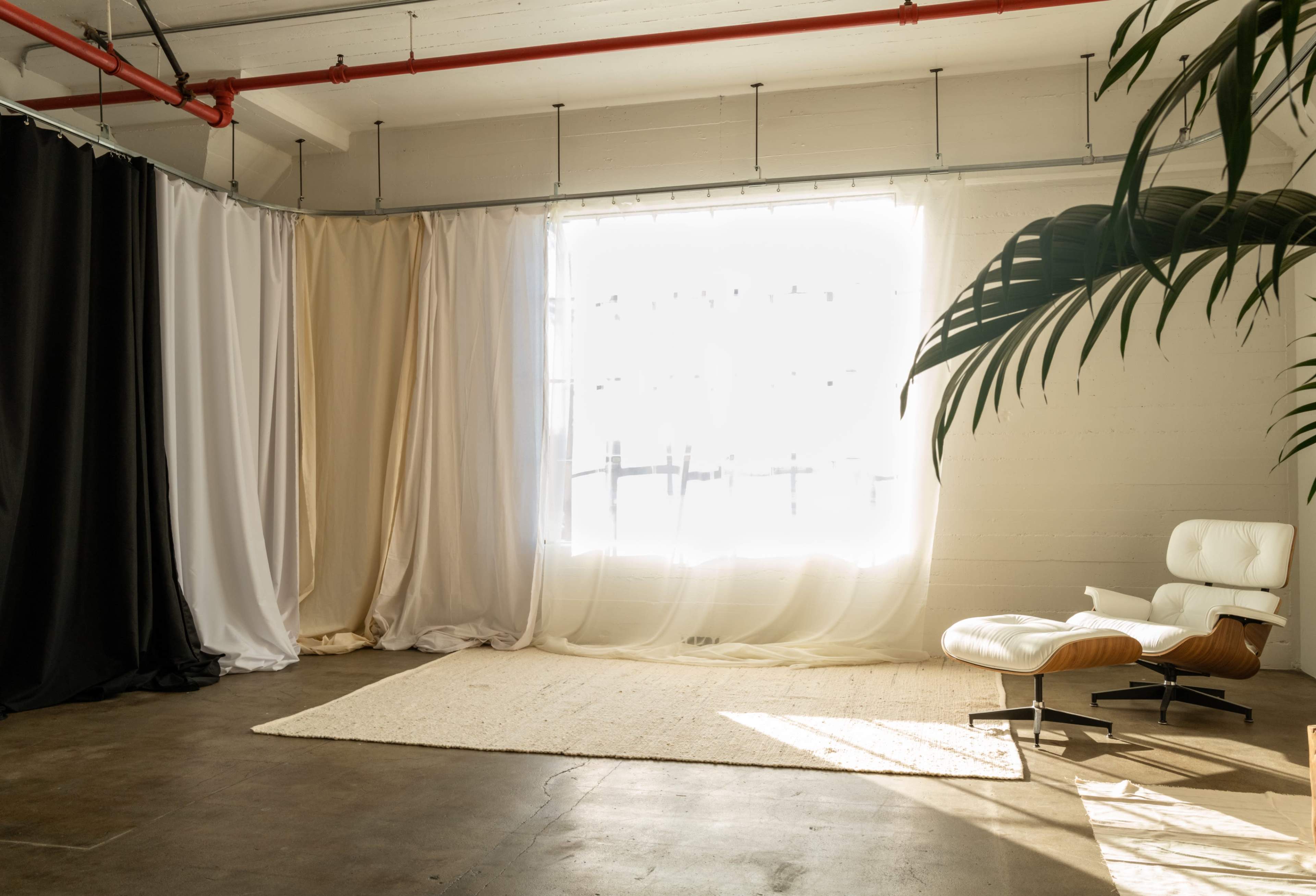 A bright, airy room with large curtains in neutral colors, a light rug on the floor, and a modern chair next to a window.