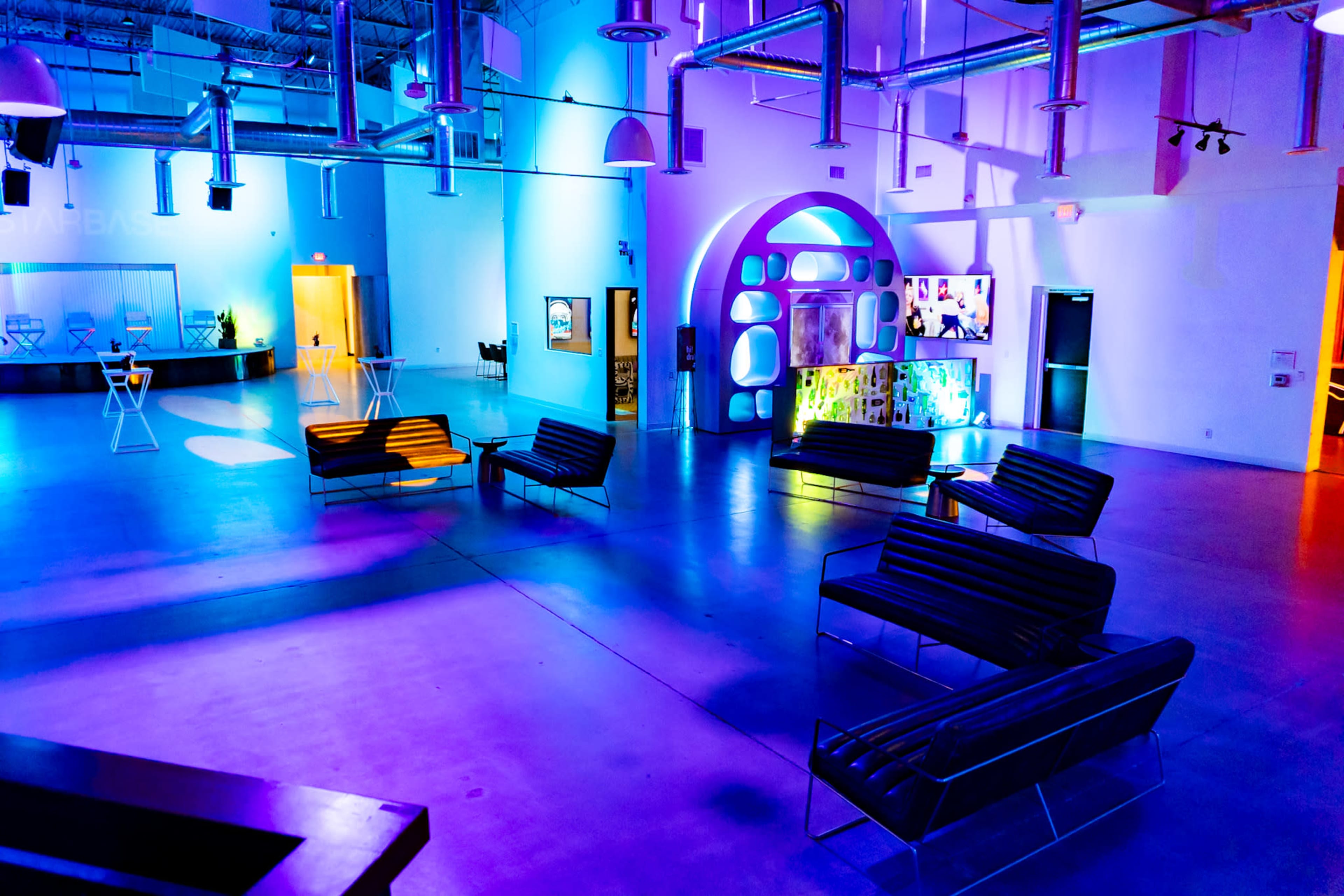 The image shows a spacious, brightly lit lounge area featuring modern furniture and colorful lighting effects.
