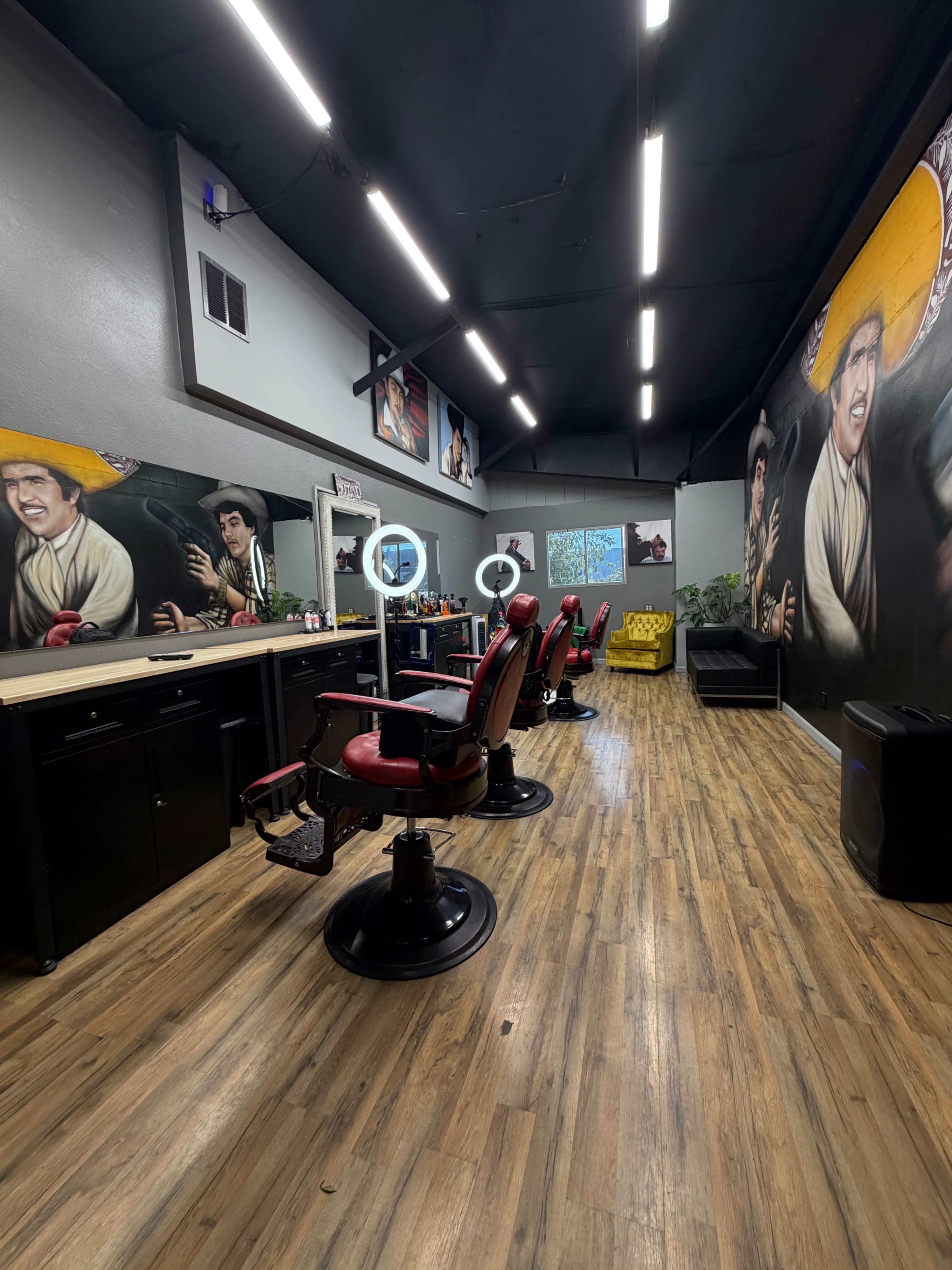 A brightly lit barbershop features several styling chairs, mirrors, and large murals on the walls.