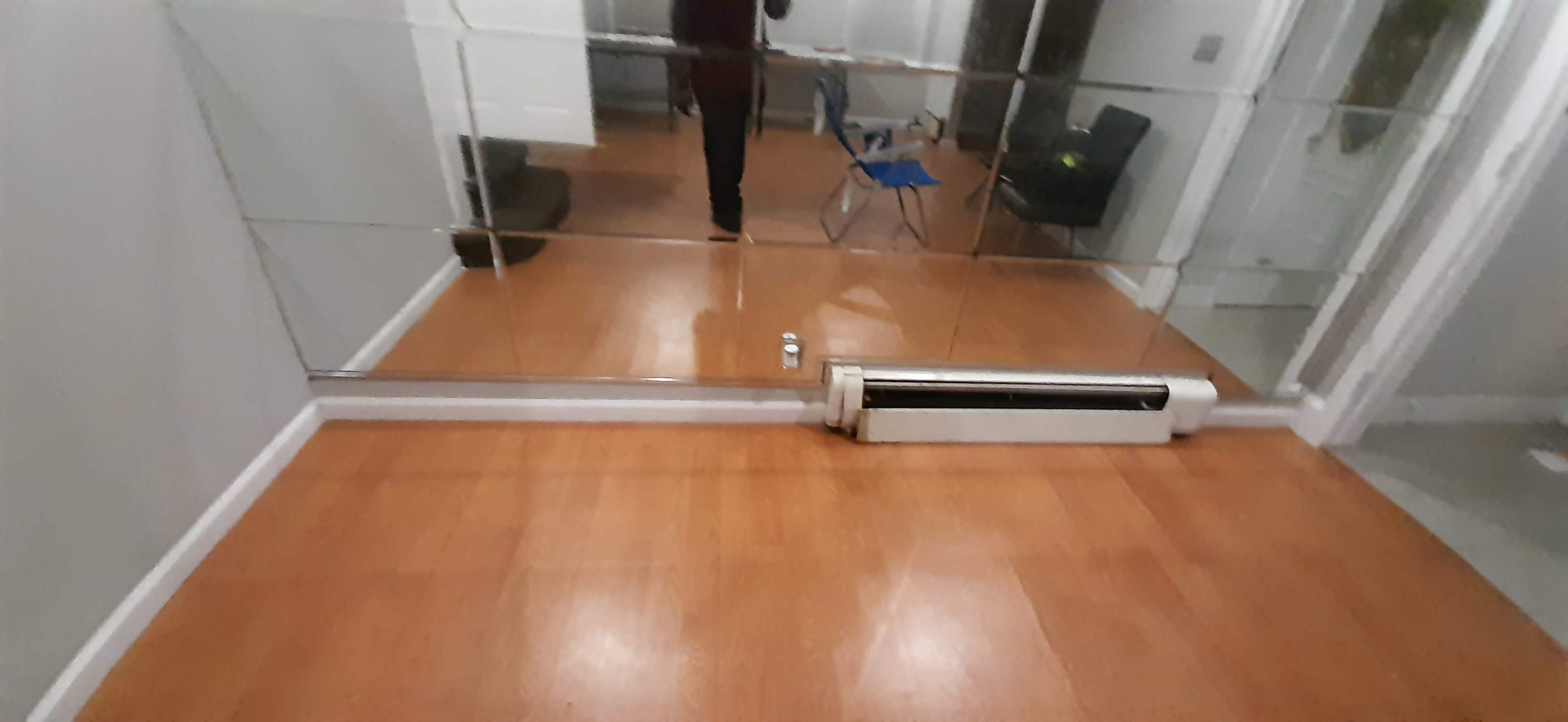 A room with hardwood flooring, a mirrored wall, and a radiator along the floor.