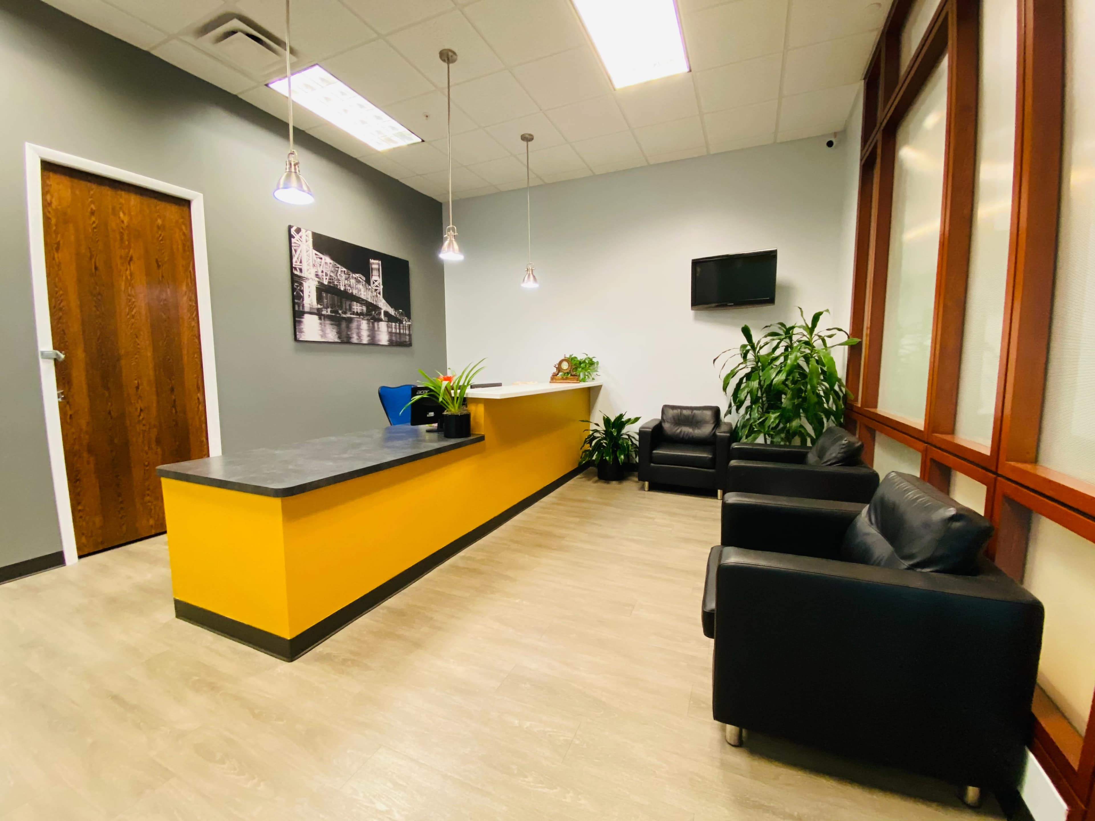A modern reception area with a yellow front desk, black leather chairs, and several green plants.