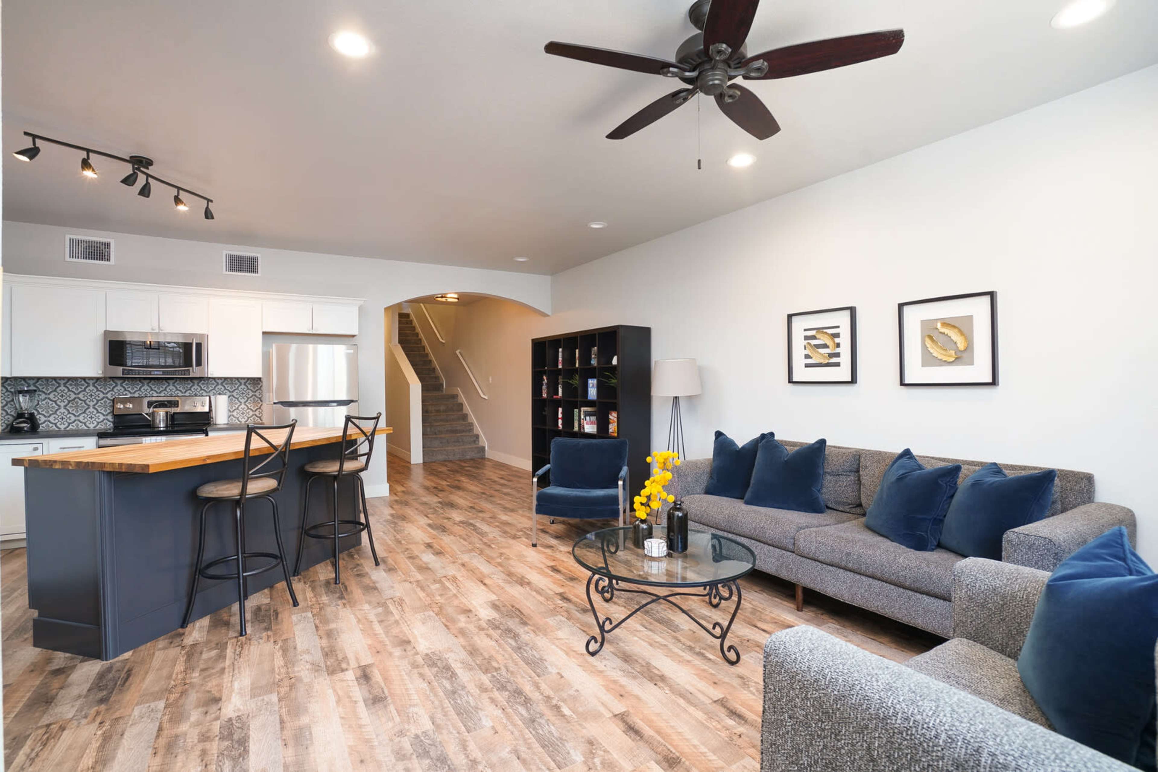 A modern living room with a gray sofa, decorative pillows, a coffee table, and a kitchen area in the background.