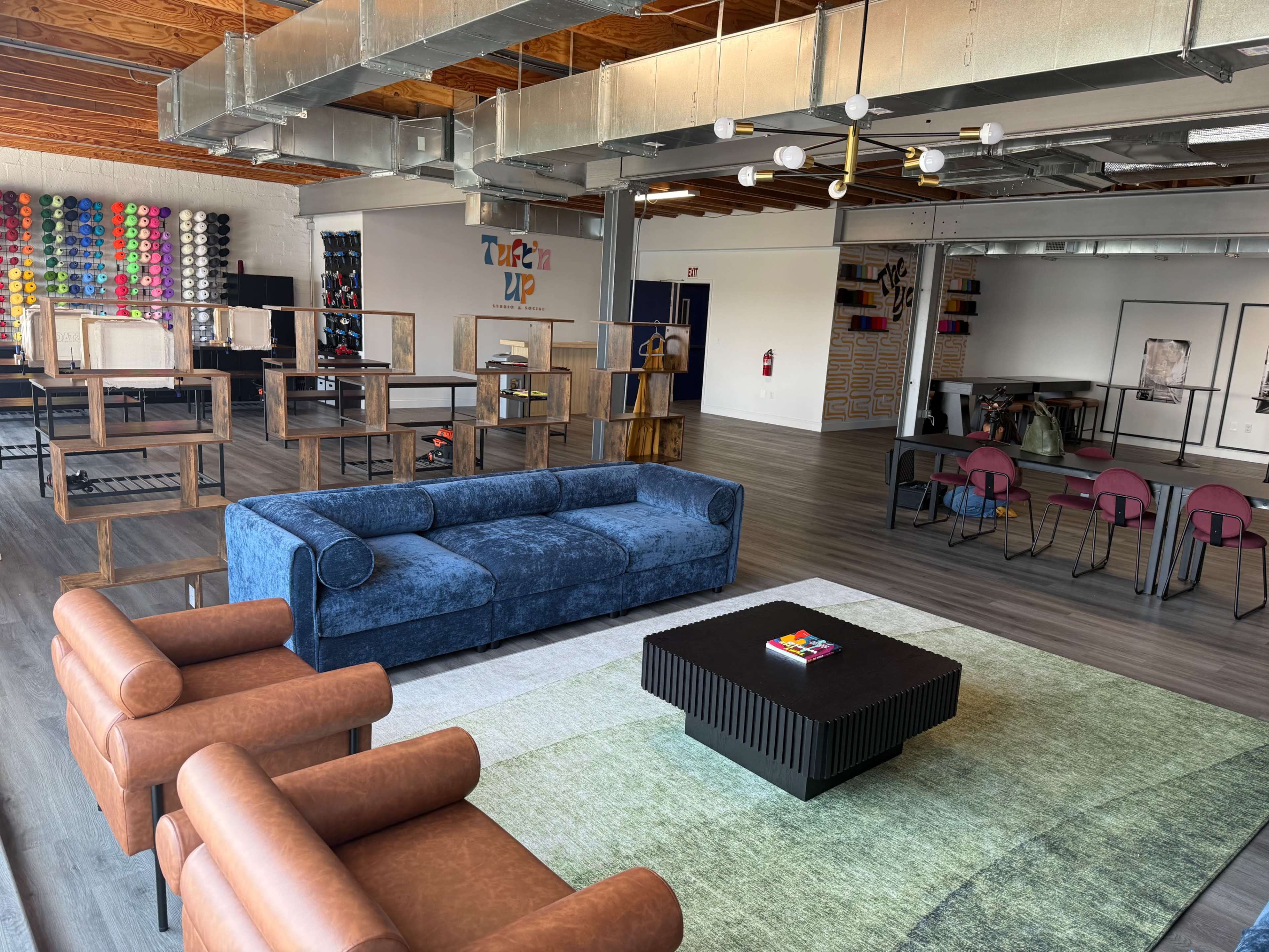 The image shows a modern open space featuring a blue couch, brown armchairs, a black coffee table, and various display shelves filled with colorful objects.