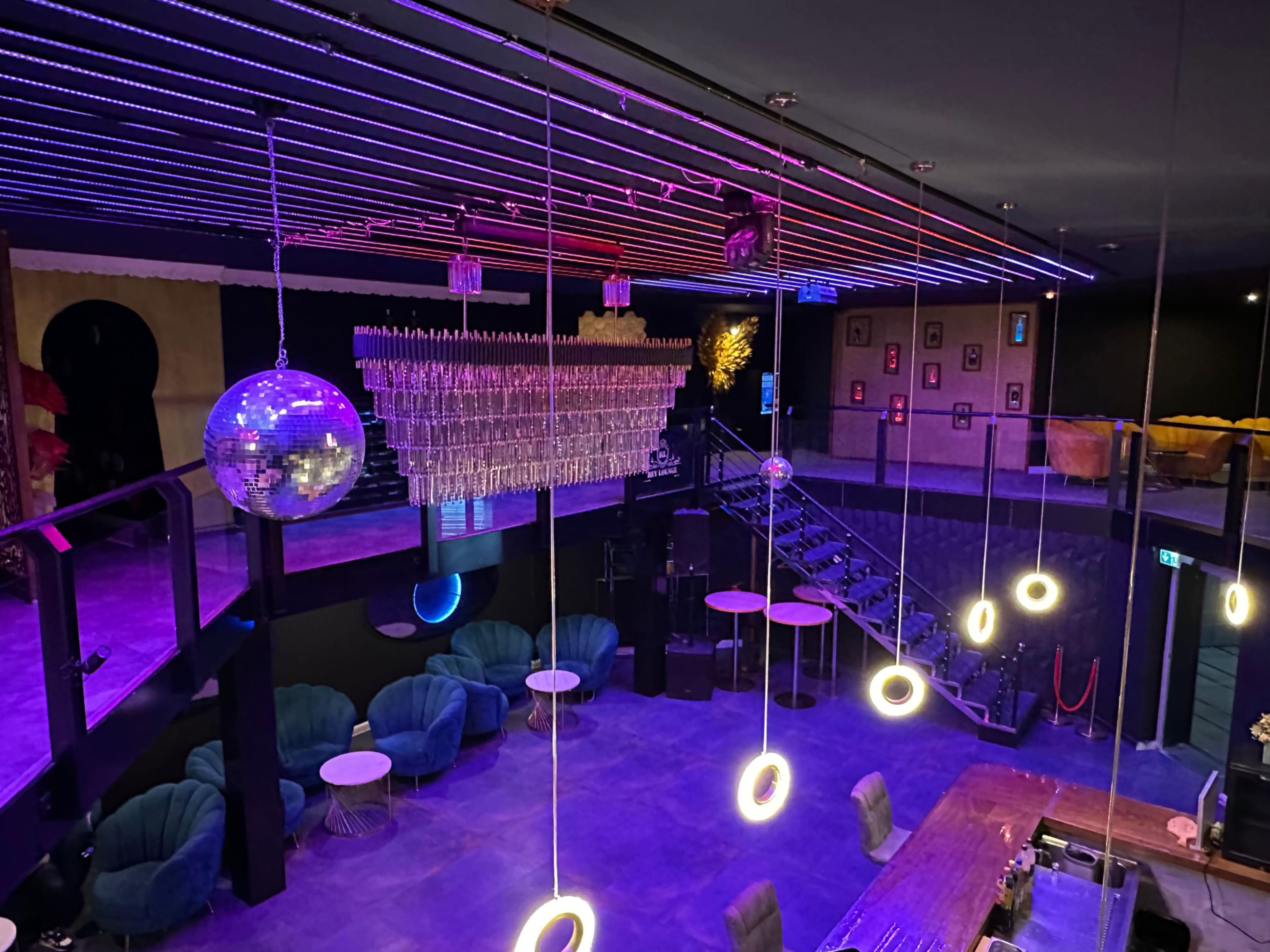 The image shows a dimly lit lounge or club with colorful lighting, a disco ball, and modern seating arrangements.