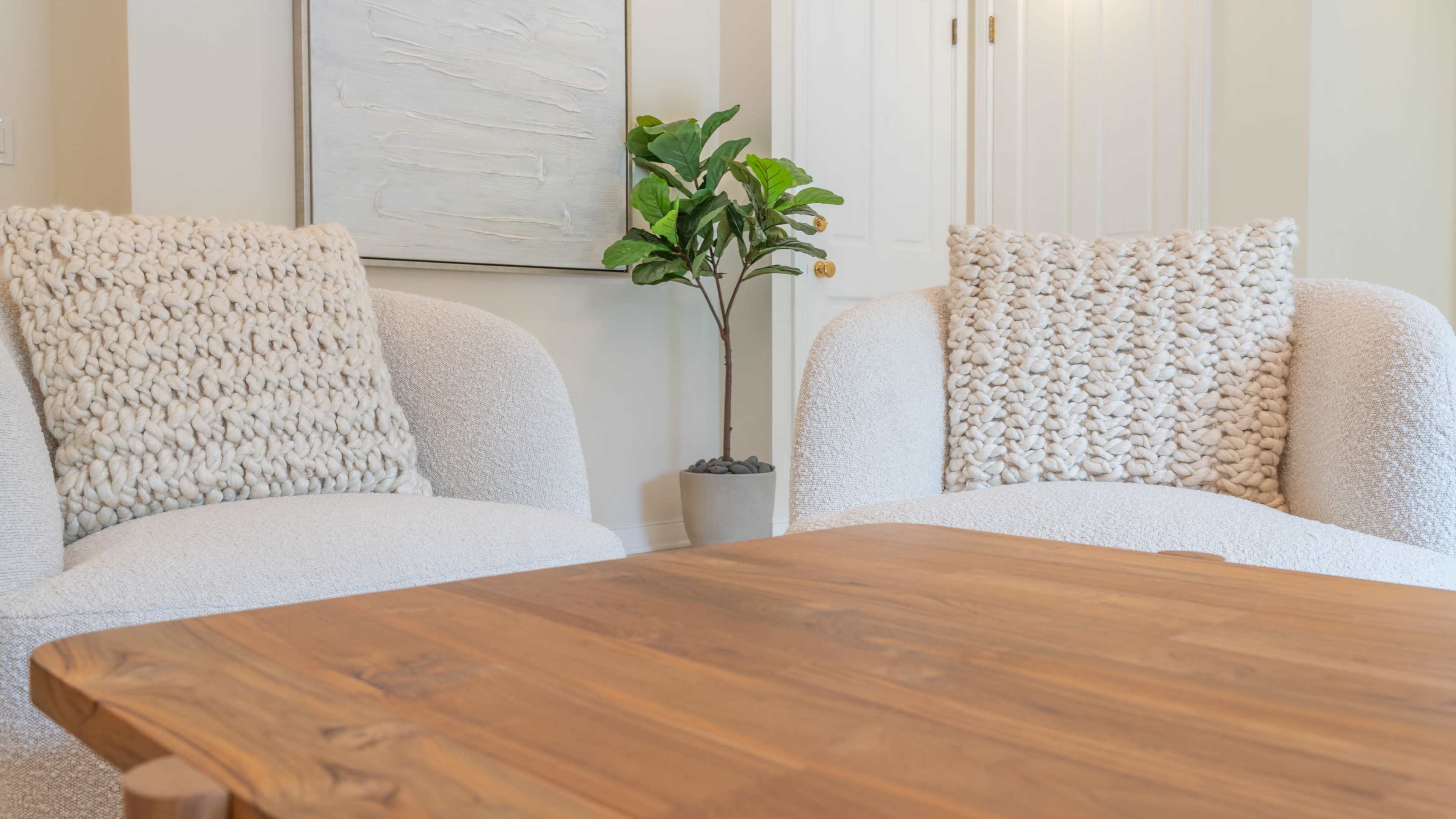 The image shows two textured white chairs facing a wooden table, with a small plant in a pot positioned nearby.