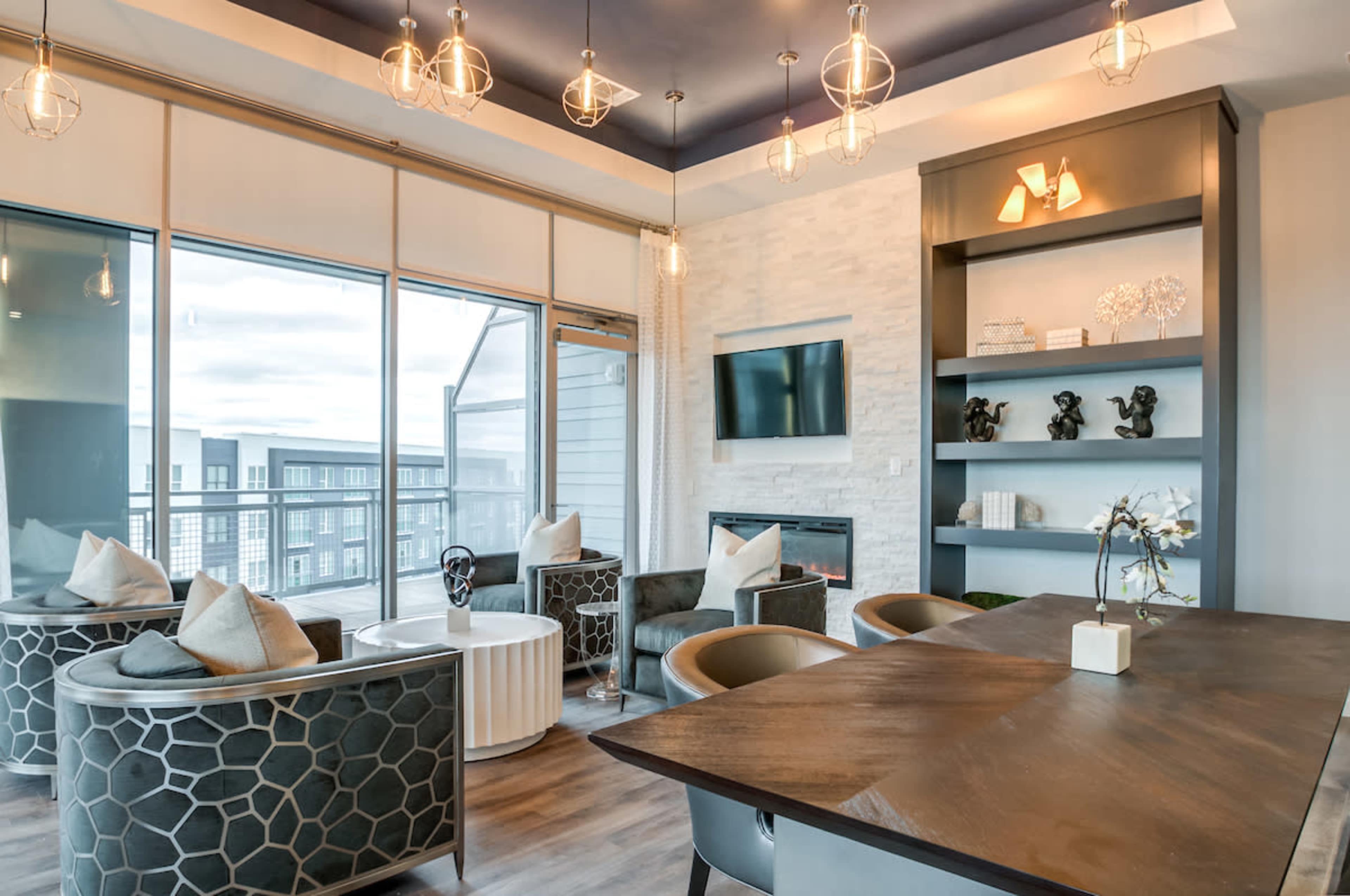 A modern lounge area with four chairs arranged around a coffee table, large windows, and a wall-mounted television.