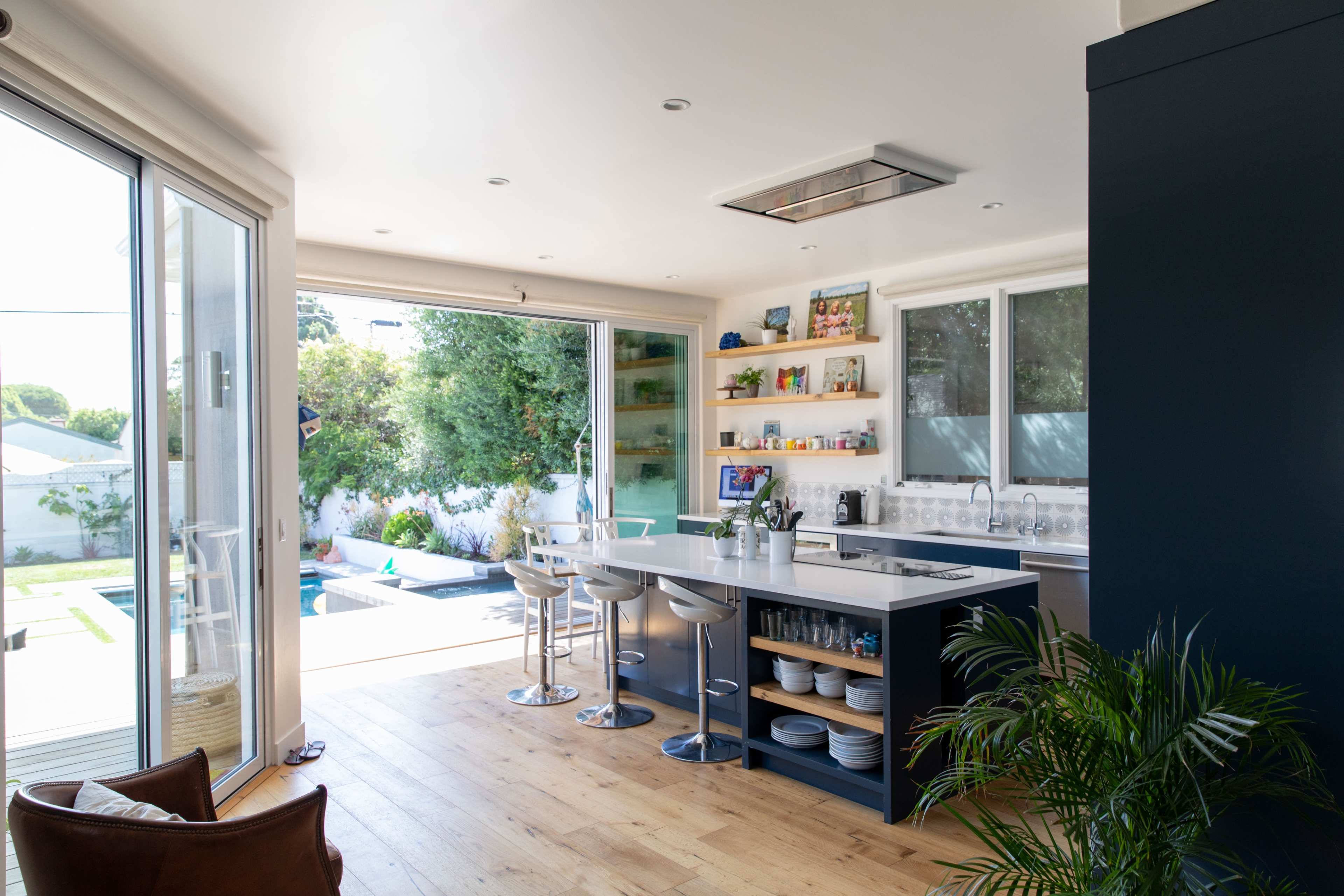 The kitchen features a modern design with a central island and bar stools, large windows opening to a patio and pool area.