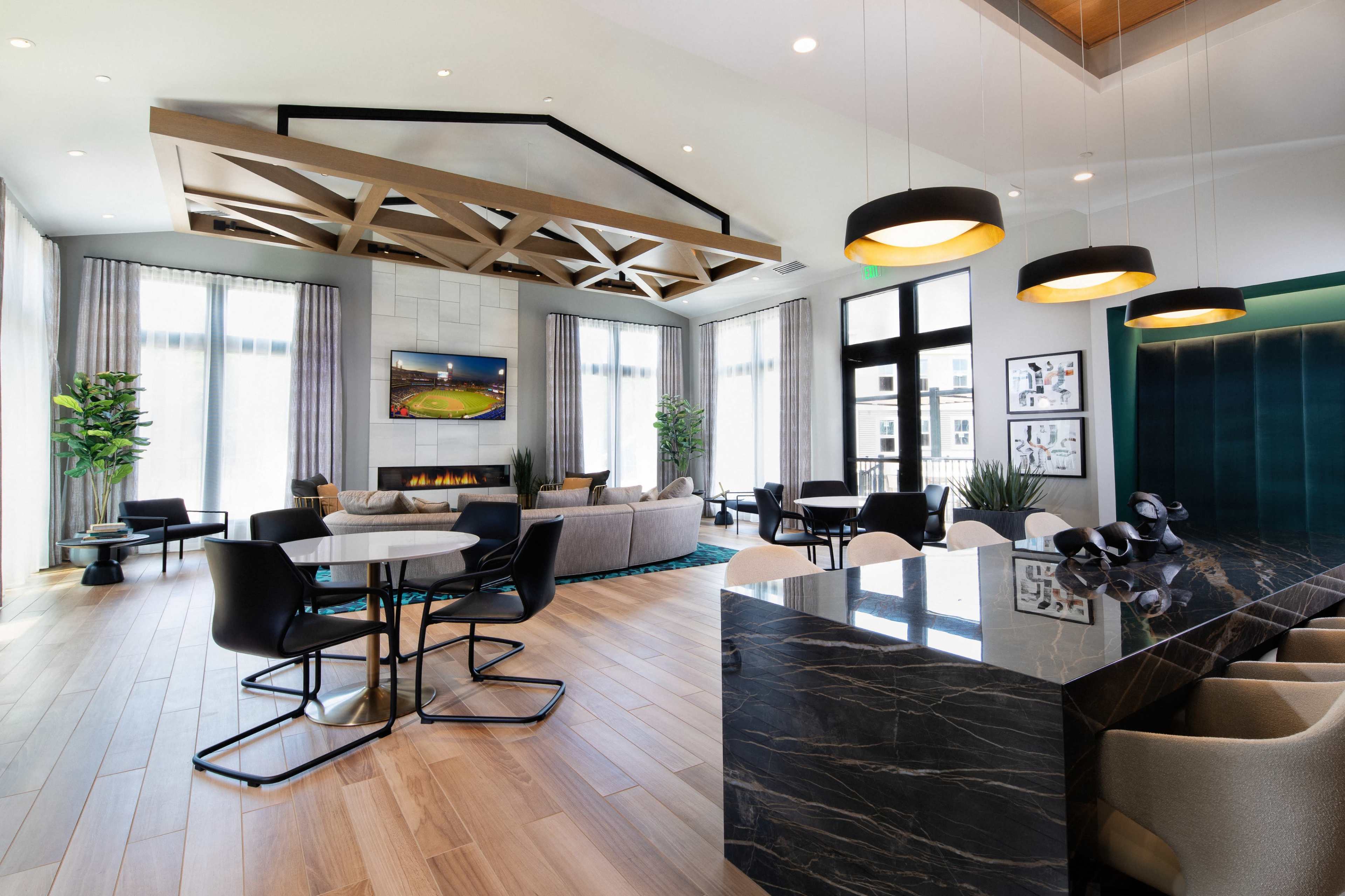 A modern communal living space featuring a seating area with a sectional sofa, a dining table, and large windows allowing natural light to fill the room.